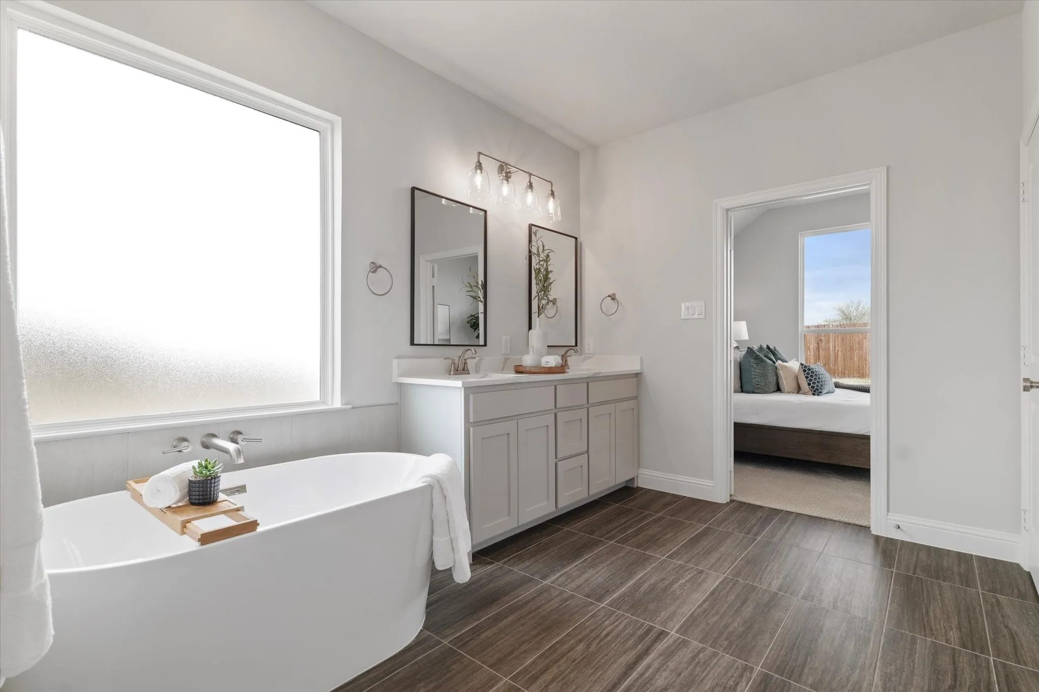 Freestanding soaking tub with wall-mounted faucet, dual vanity with undermount sinks, and wood-look tile flooring