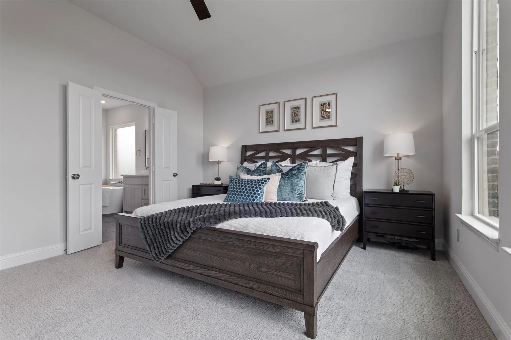 Vaulted ceiling, light neutral wall color, plush carpet flooring, double doors to bathroom, and window with white trim