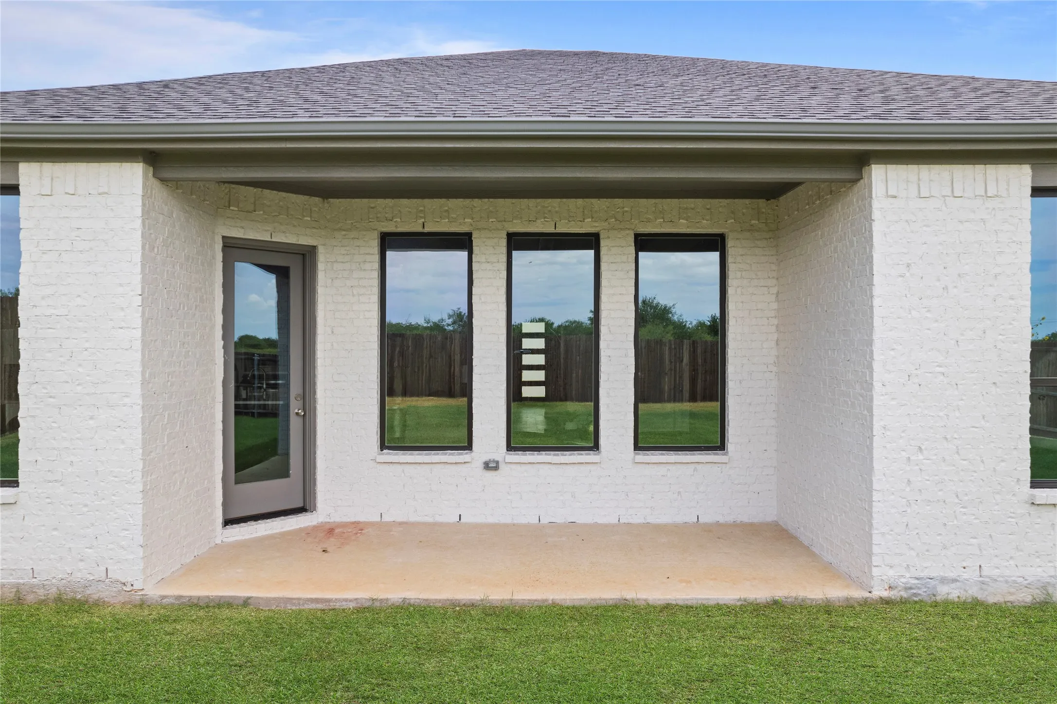 Covered patio with a concrete slab, white painted brick exterior, and a full-light glass door
