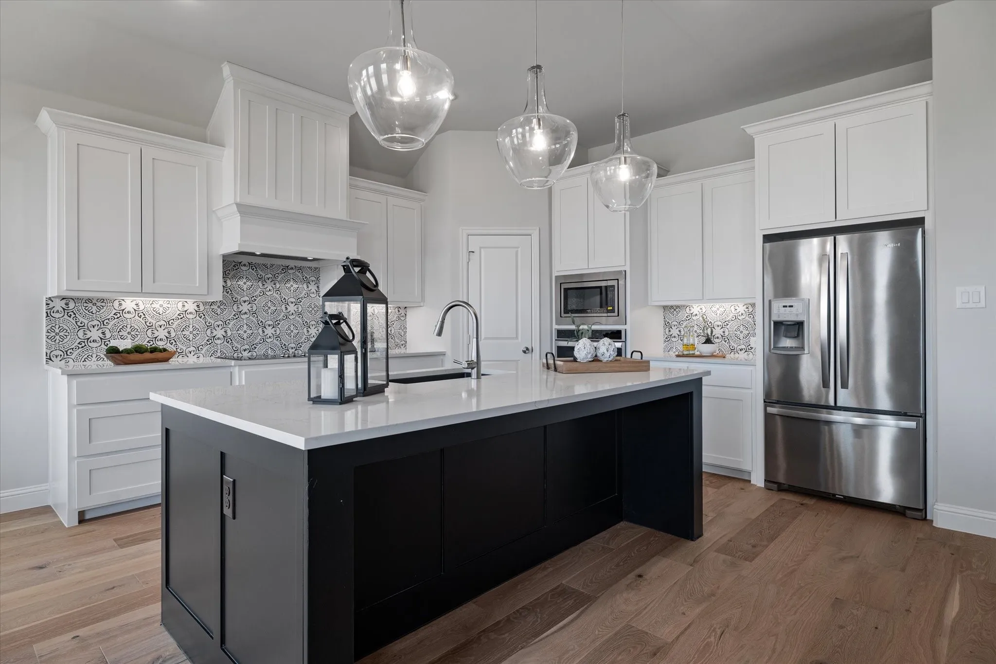 Kitchen featuring white upper cabinetry, a dark-toned island with a light-colored countertop, stainless steel appliances, a decorative tile backsplash, and wood-finish flooring
