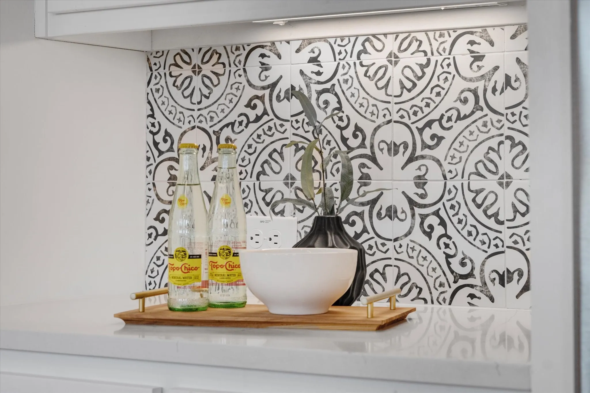 White upper cabinetry, under-cabinet lighting, patterned tile backsplash, solid surface countertop, and electrical outlets