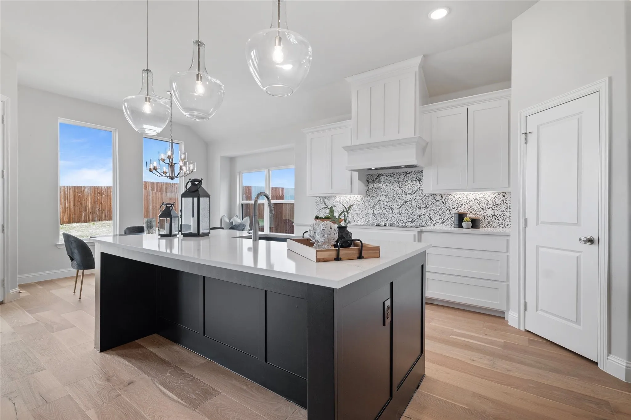 Kitchen featuring a dark-toned island with a light-toned quartz countertop, white cabinetry, a patterned tile backsplash, and light wood-finish flooring