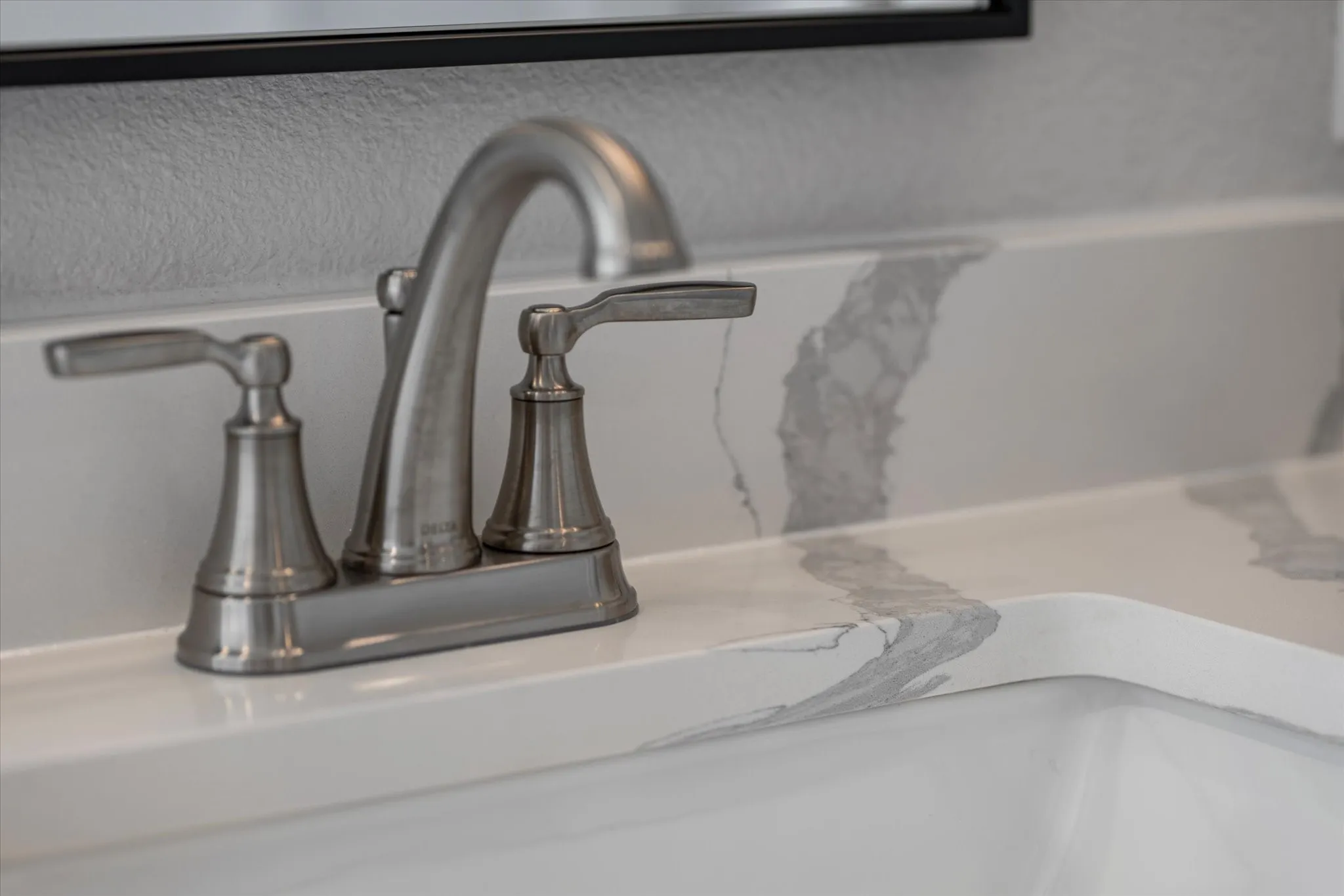 Brushed nickel two-handle faucet with a white vanity top featuring gray veining and an integrated sink