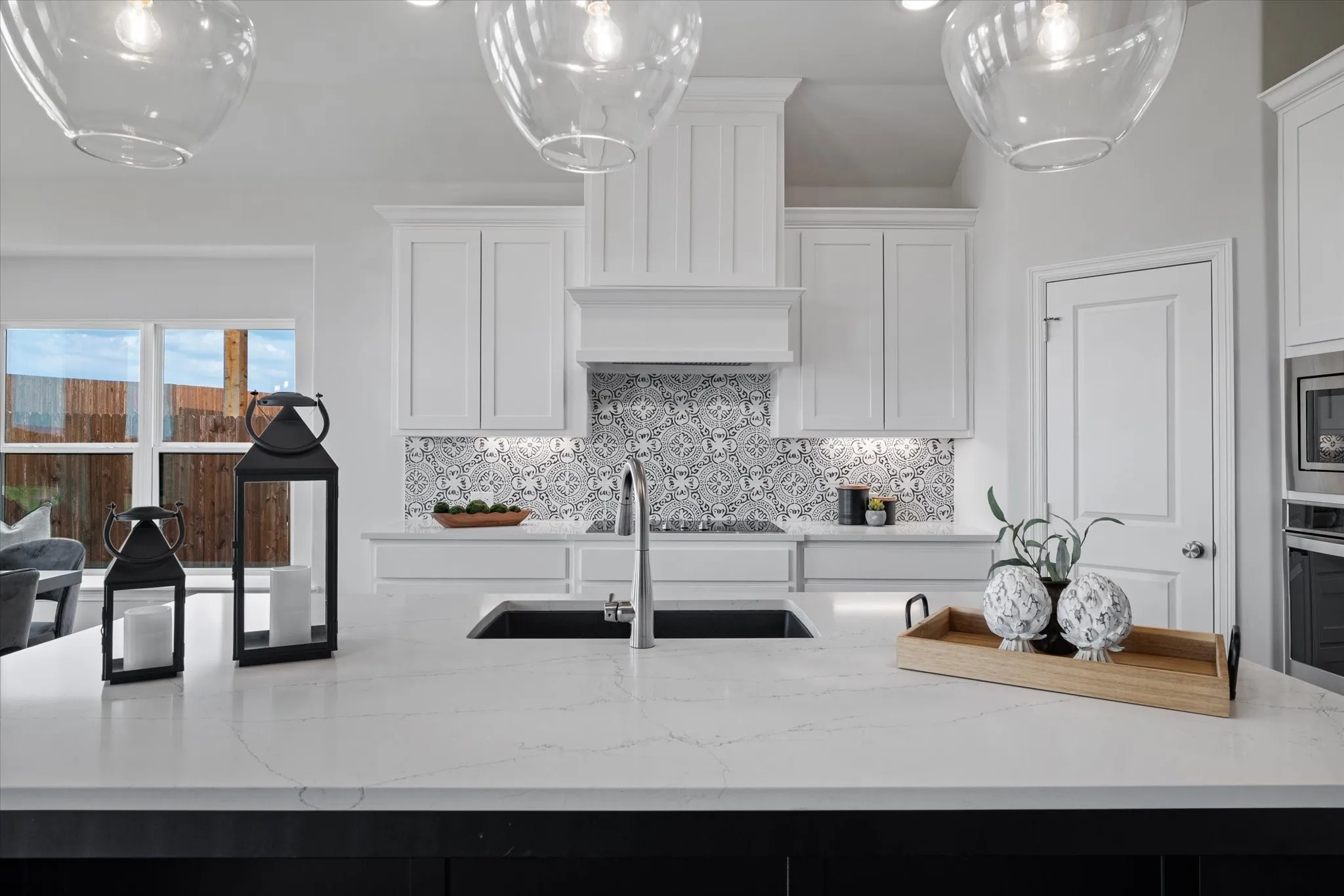 Kitchen featuring white cabinetry, a decorative tile backsplash, a stainless steel sink, built-in stainless steel appliances, and a large central island with a light-toned quartz countertop