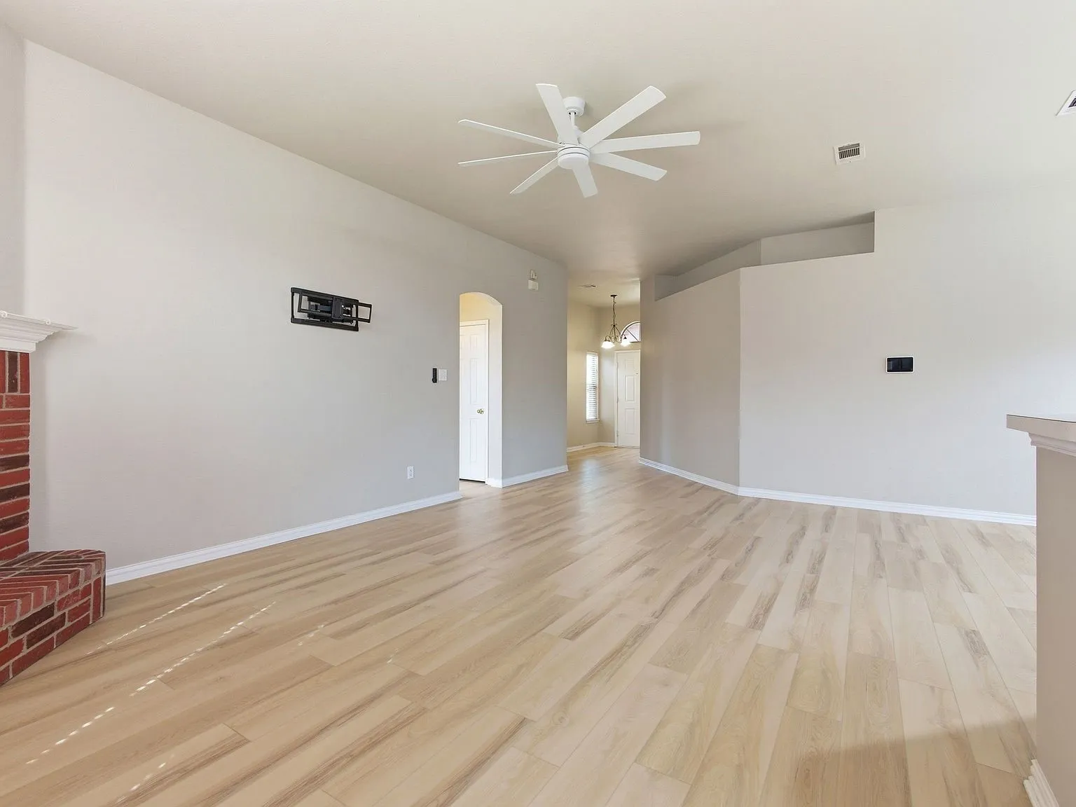 Open-concept floor plan with light wood-finish flooring, a white ceiling fan, and a brick-finish fireplace with a decorative mantel