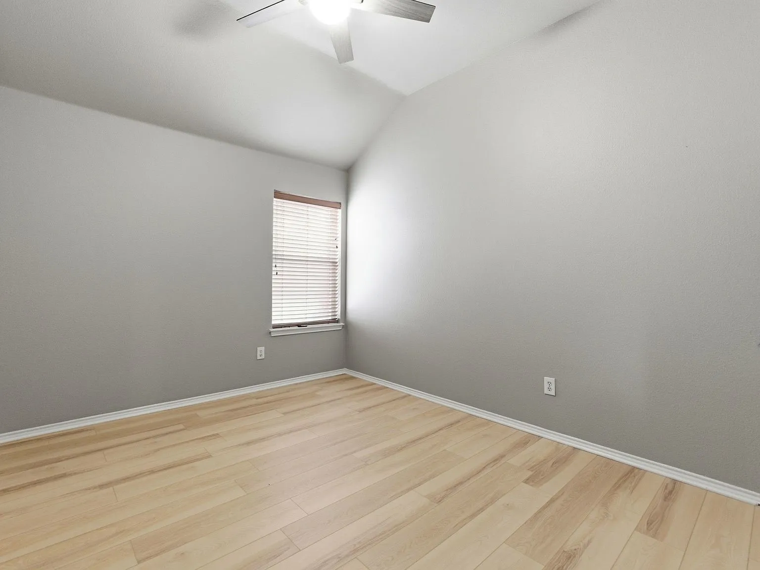 Vaulted ceiling, wood-finish flooring, ceiling fan, window with blinds, light gray wall paint
