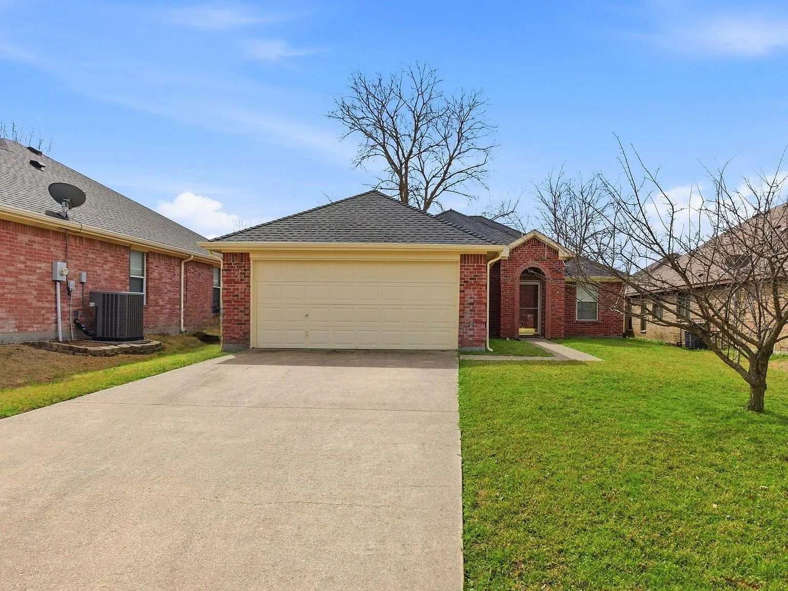 Brick exterior with an arched entry, attached garage, concrete driveway, and front lawn