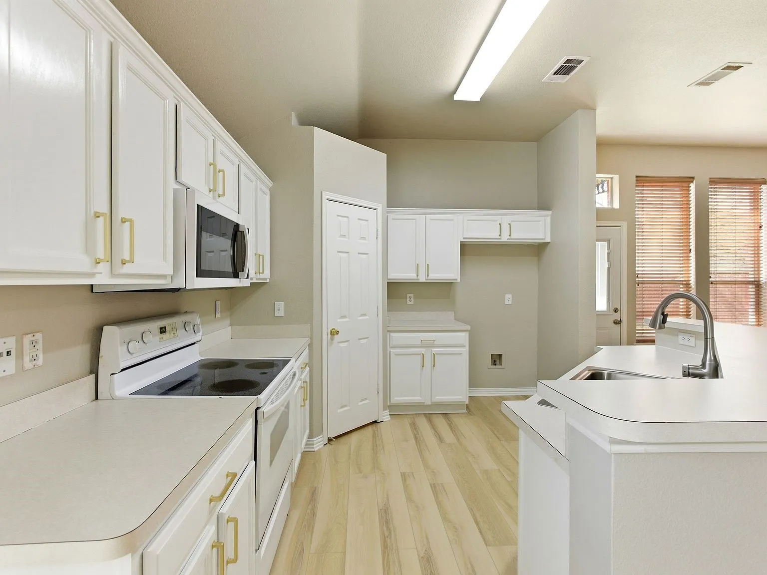 Kitchen featuring white cabinetry with gold-tone hardware, a stainless steel sink with a gooseneck faucet, light-toned flooring, and an electric range