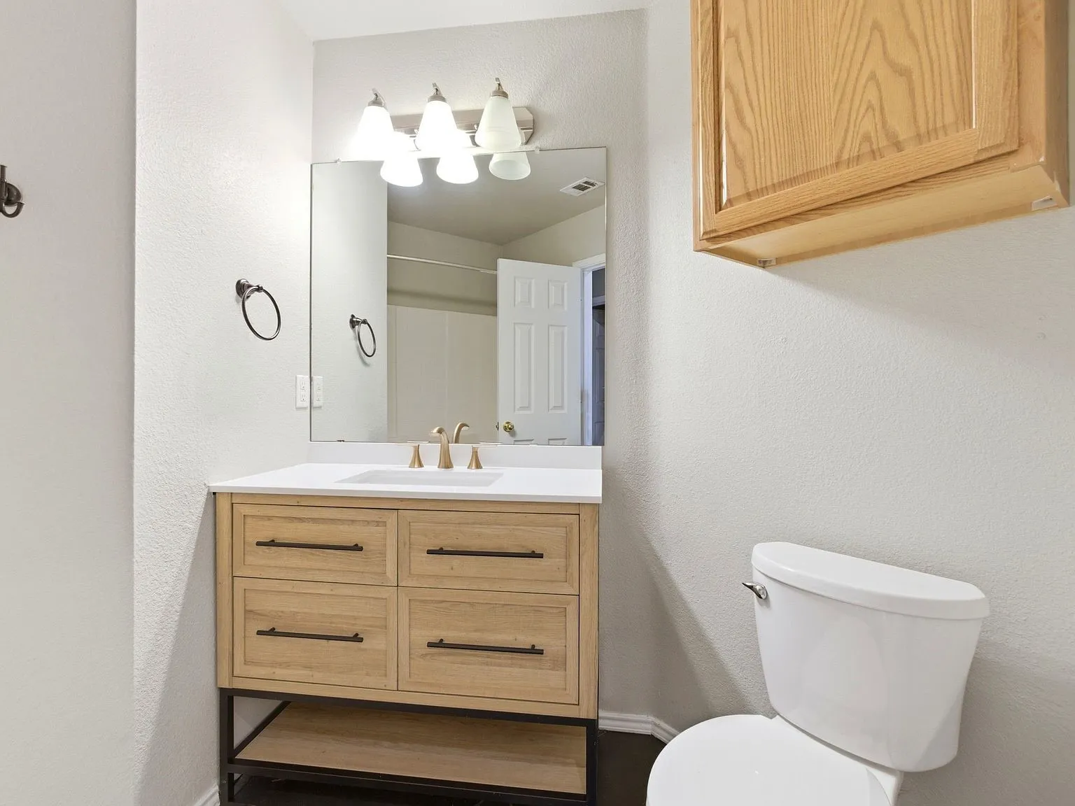 Wood-finish vanity with drawer storage, white countertop with integrated sink, gold-tone faucet, and overhead lighting fixture