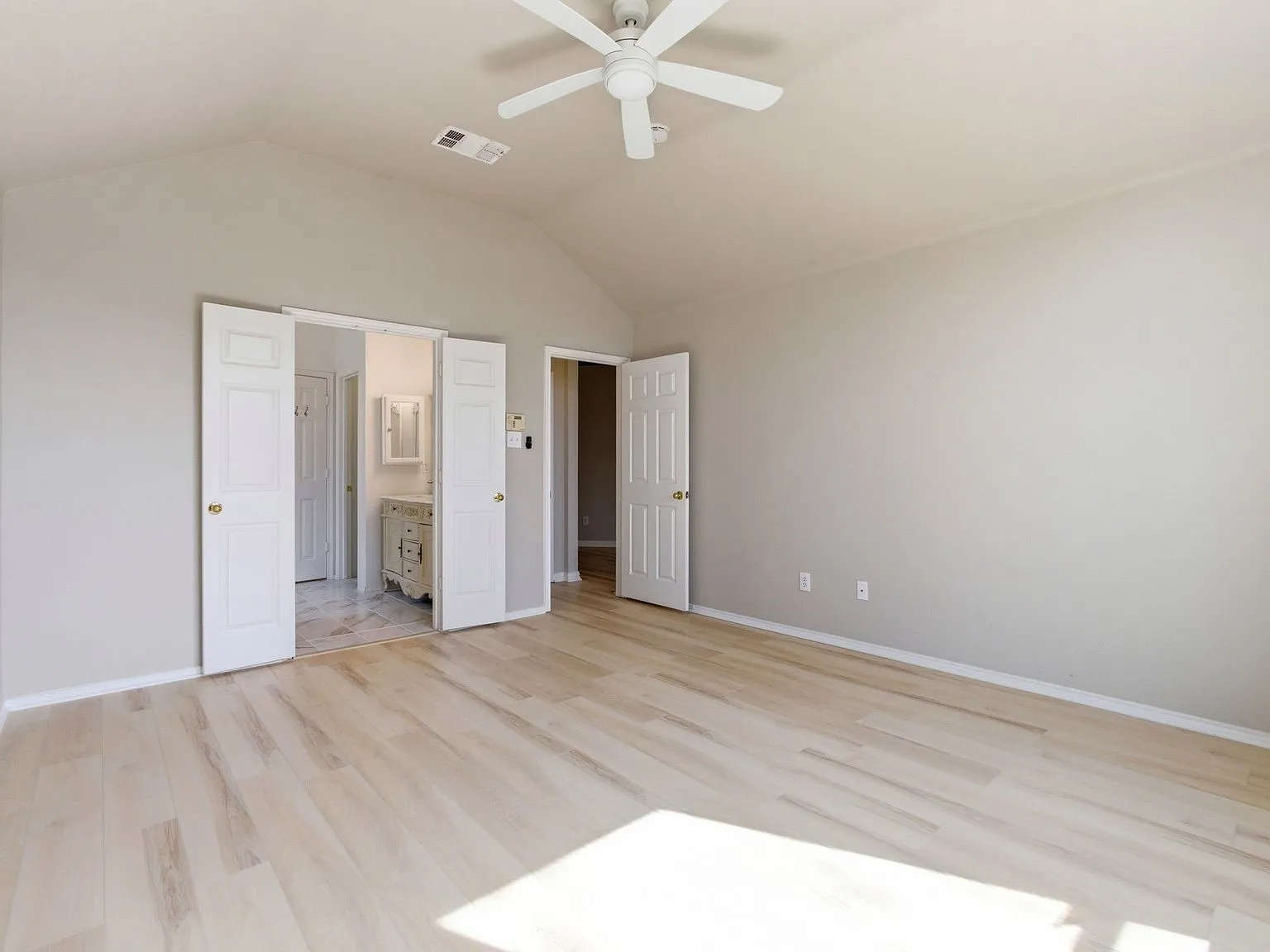 Vaulted ceiling with a ceiling fan, light wood-finish flooring, and white paneled doors