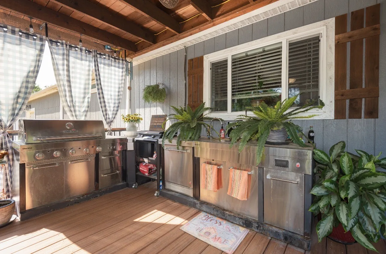 Covered outdoor patio featuring wood-finish decking and a built-in outdoor kitchen with stainless steel appliances