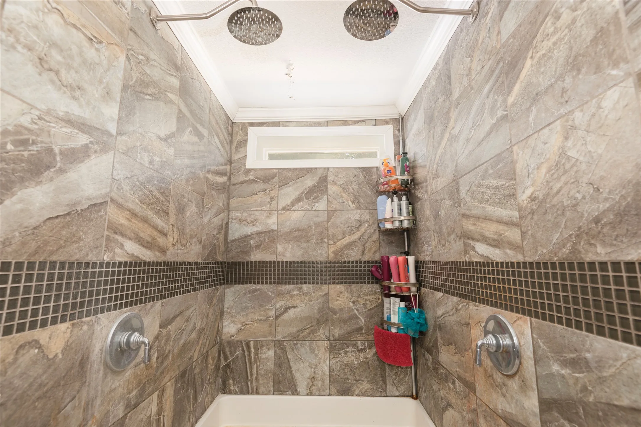 Tiled shower with dual rain shower heads, mosaic tile accent band, and a transom window