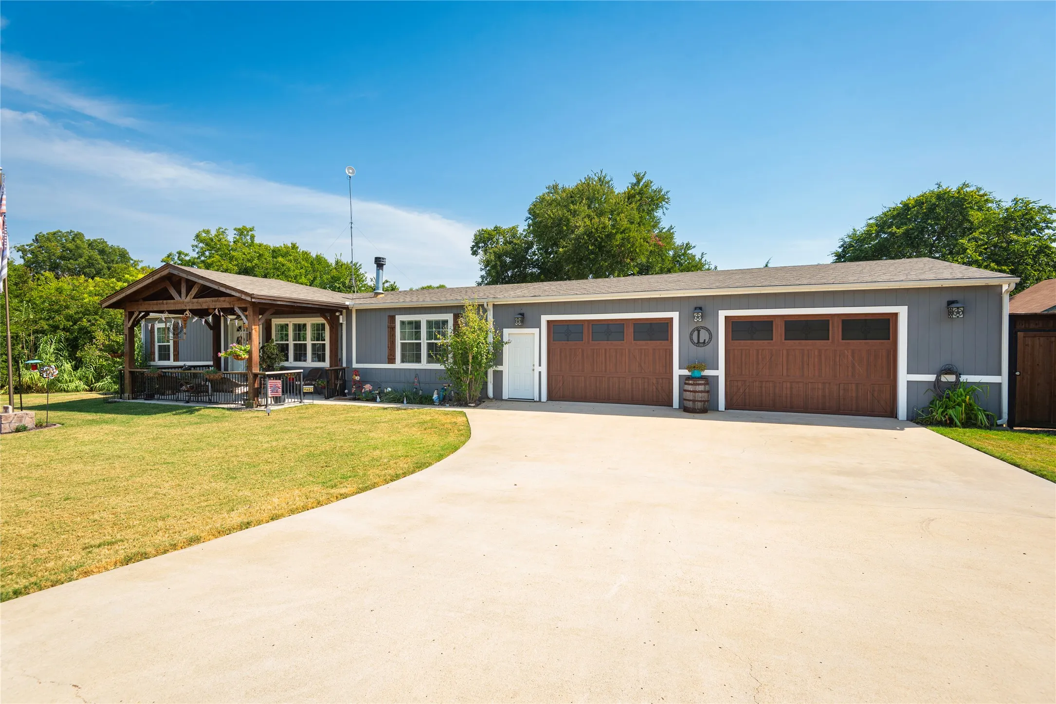 Expansive concrete driveway, attached two-car garage with wood-finish doors, covered front porch with exposed timber framing, gray siding exterior