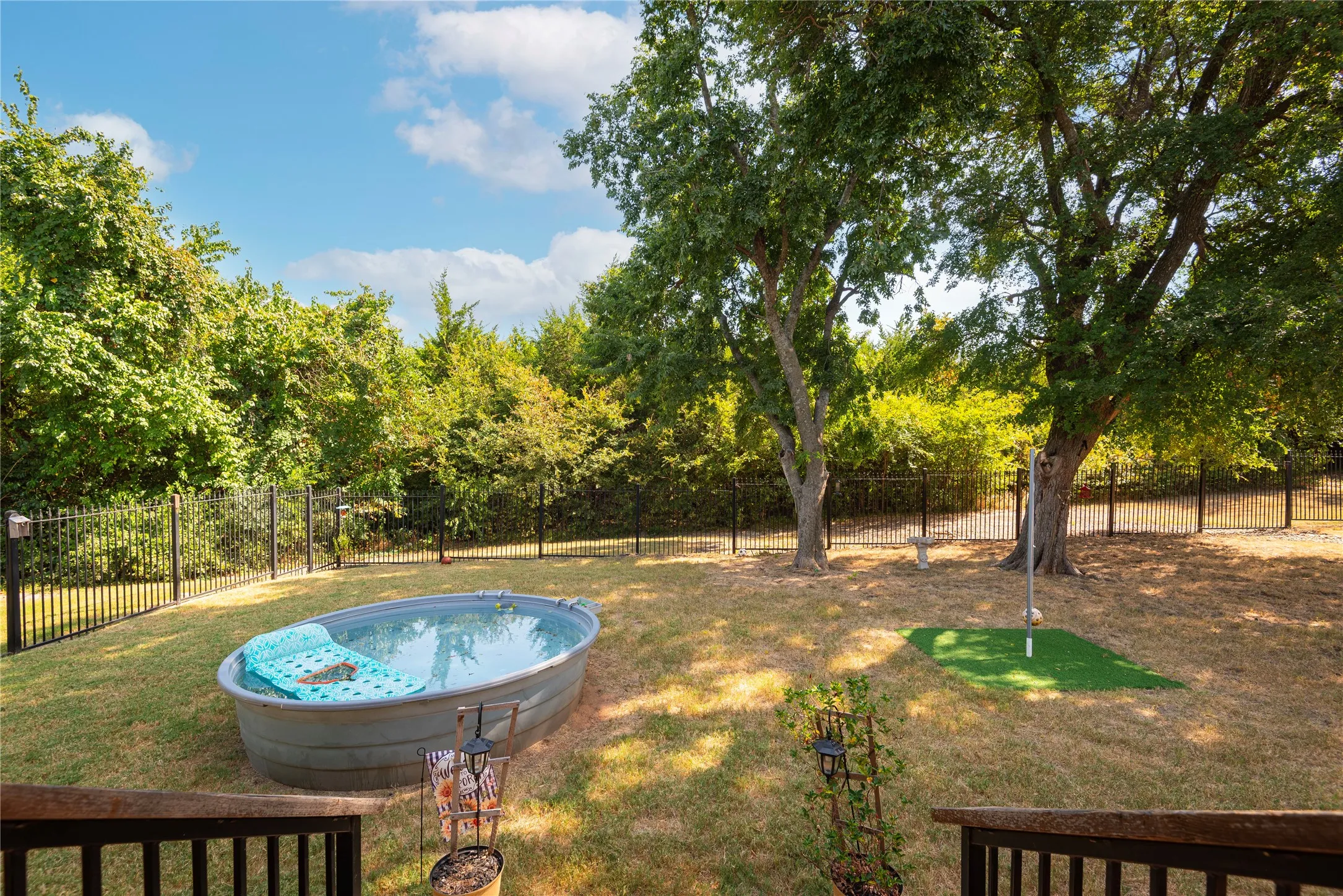 Fenced backyard featuring mature trees, a stock tank pool, and a dedicated artificial turf area