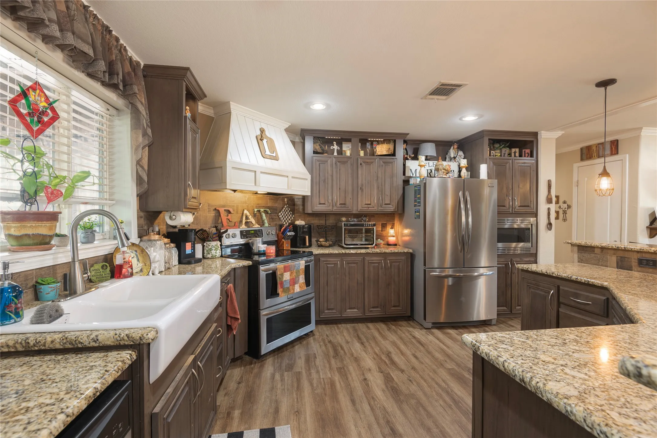 Kitchen featuring wood-finish flooring, granite countertops, wood cabinetry, a farmhouse sink, and stainless steel appliances