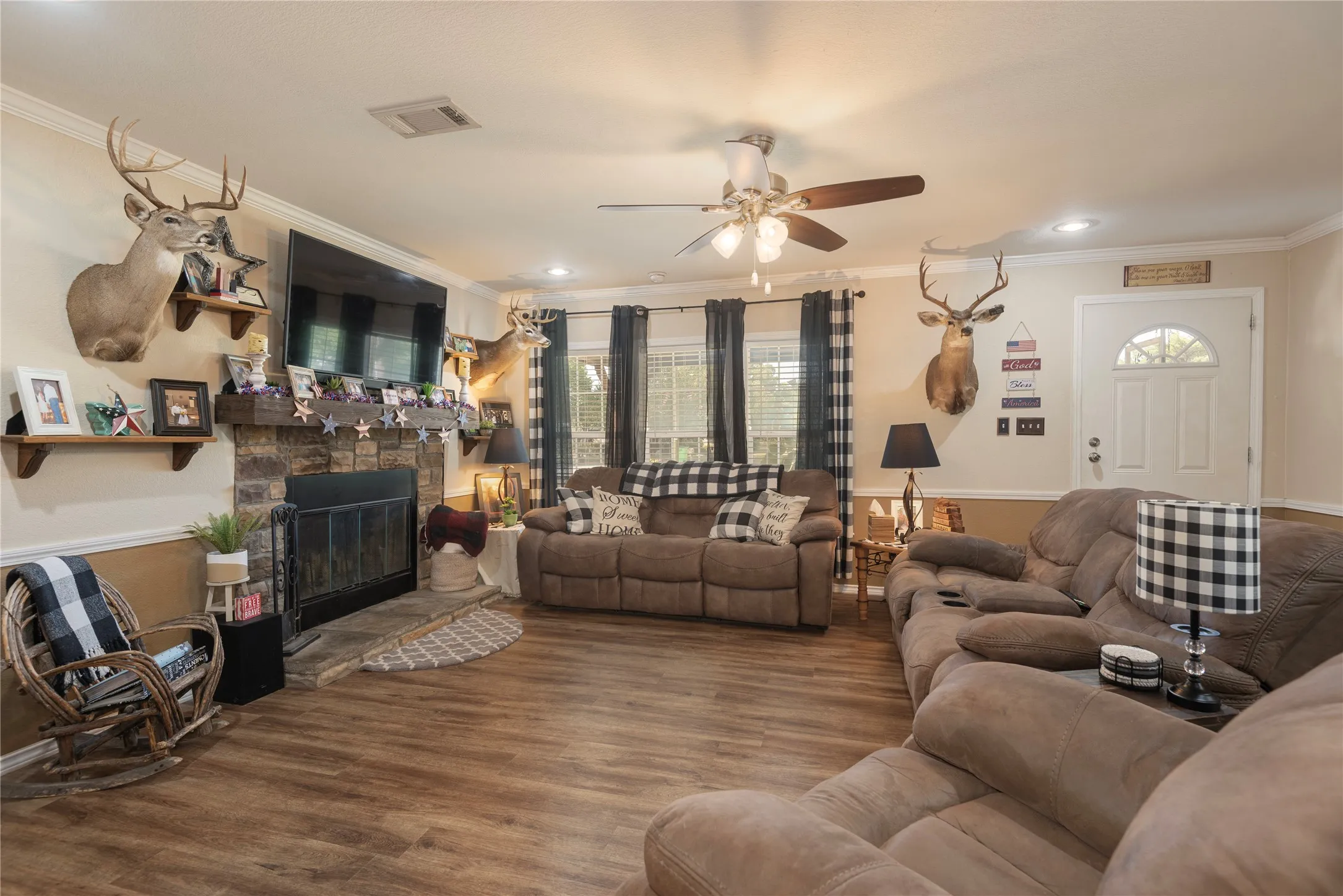 Living space featuring wood-finish flooring, a stone-surround fireplace with a wood mantel, crown molding, and a ceiling fan