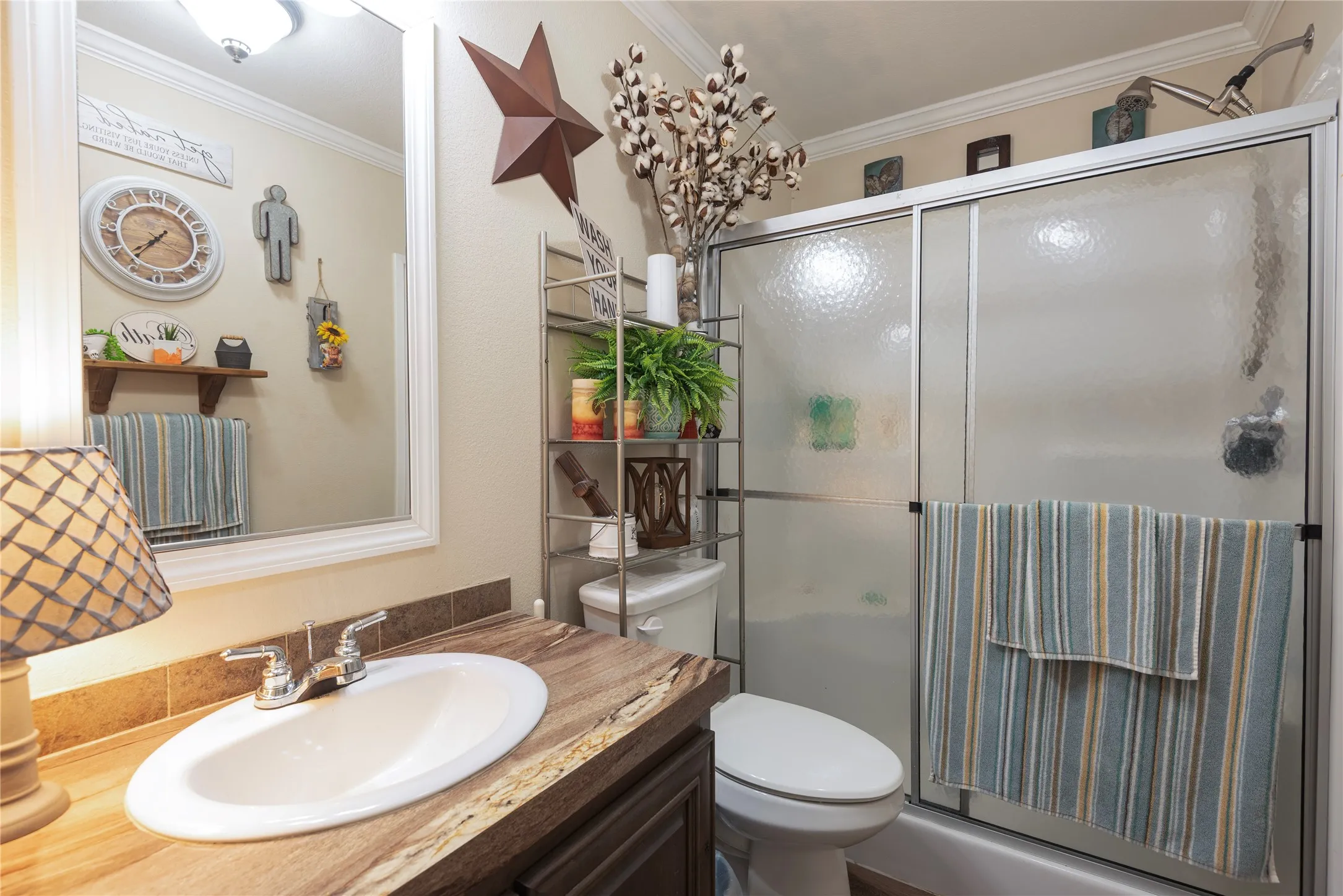 Bathroom featuring a built-in vanity with an undermount sink, a chrome two-handle faucet, a framed wall mirror, a shower with a sliding glass enclosure, and crown molding