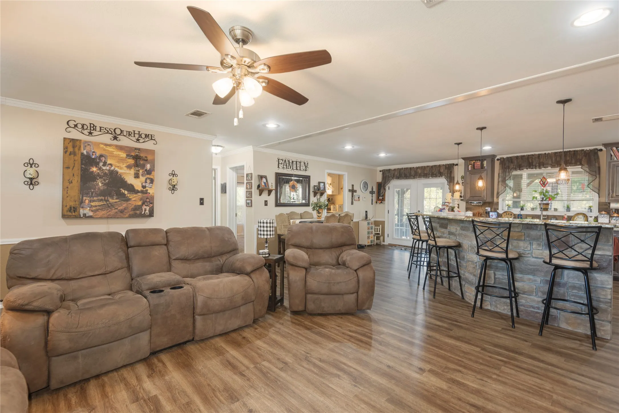 Open-concept living area featuring wood-finish flooring, a stone-clad kitchen island with pendant lighting, and French doors