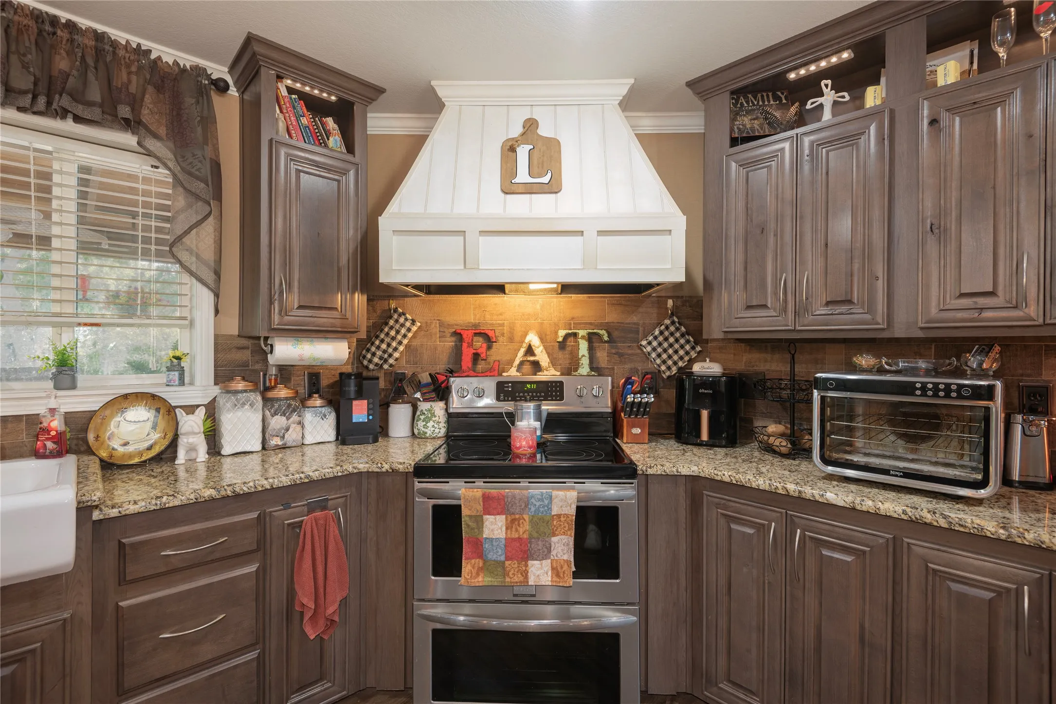 Kitchen featuring wood-finish cabinetry, stone countertops, stainless steel appliances, a white farmhouse sink, and a white range hood