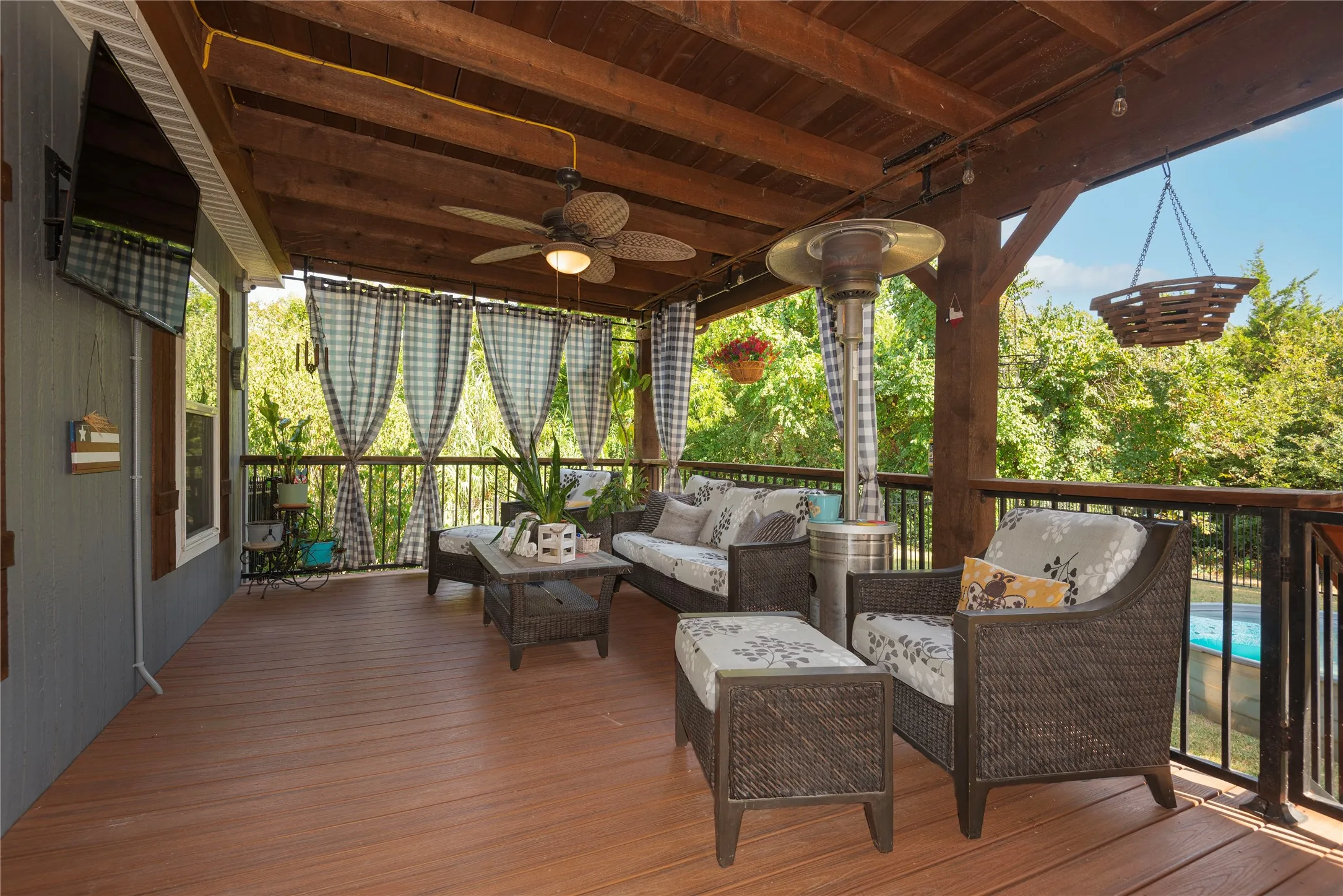 Covered wood-finish deck with exposed beam ceiling, ceiling fan, and black metal railings
