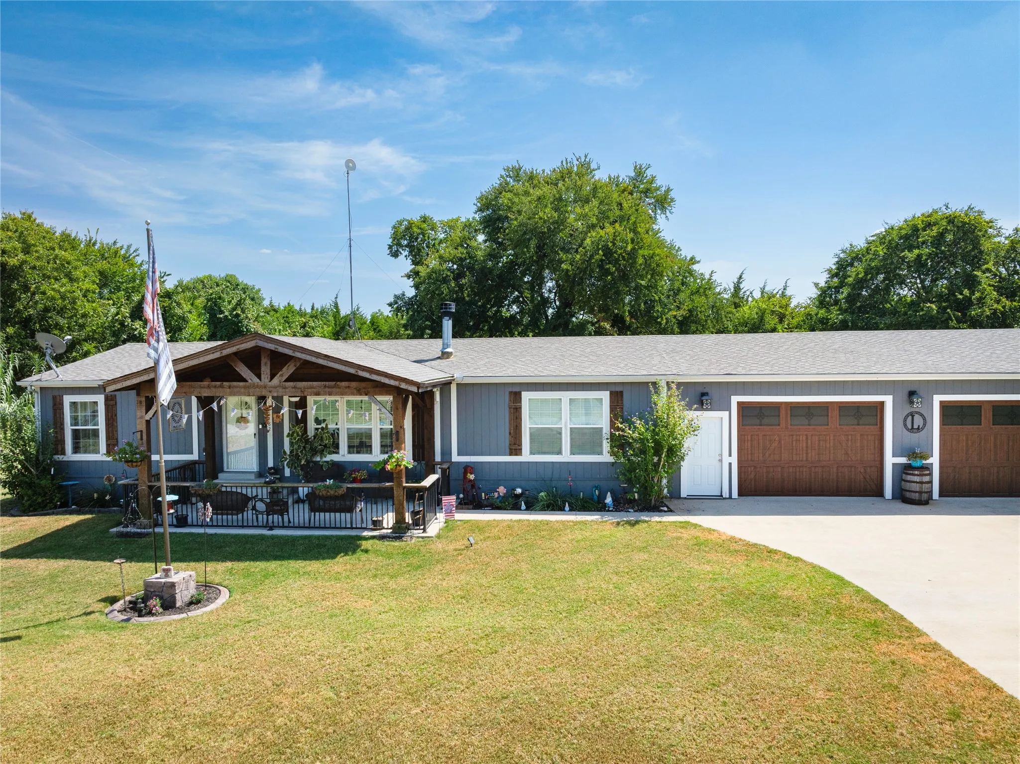 Light gray siding residence with a covered front porch featuring exposed wood beams, white trim, and a concrete driveway