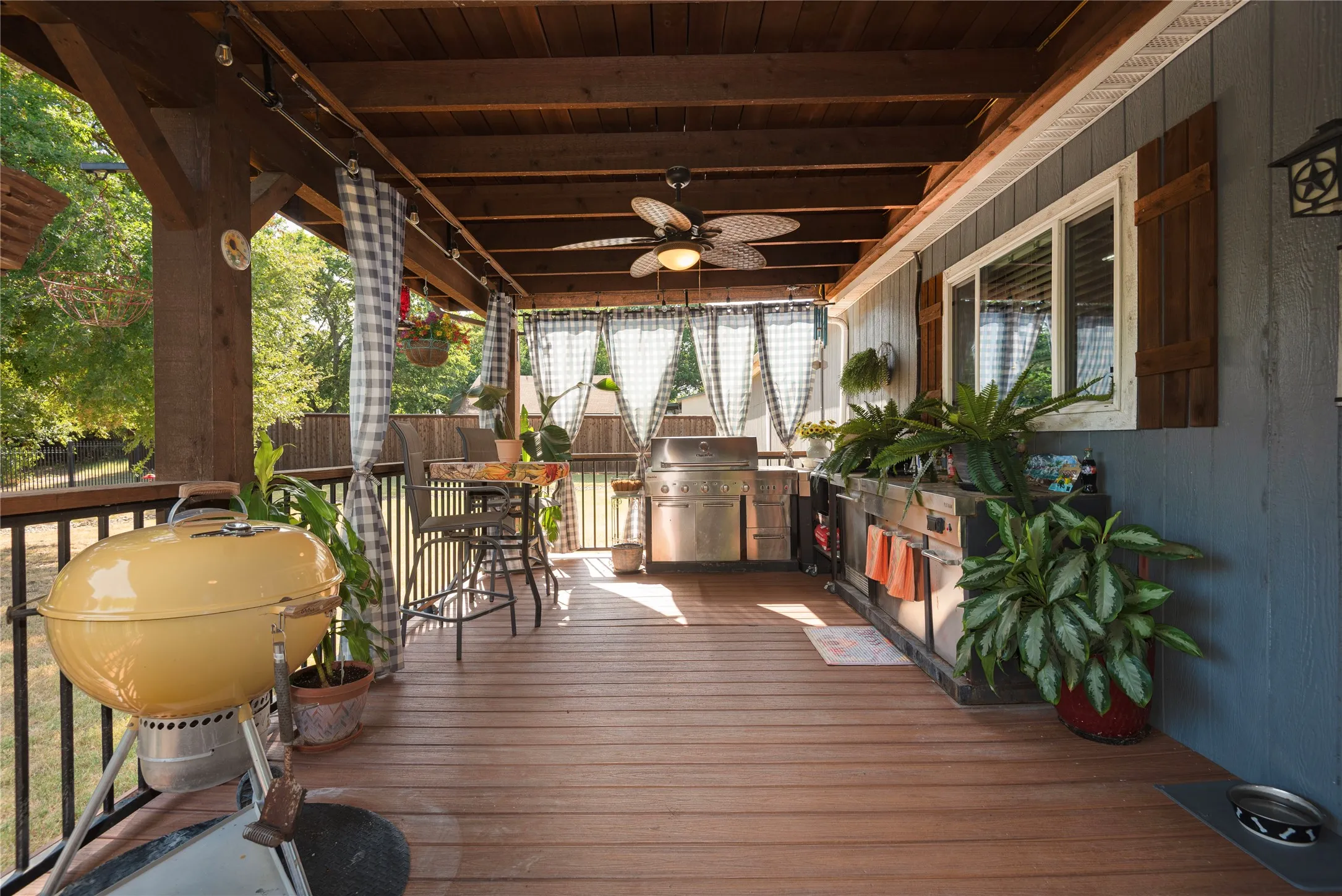 Expansive covered deck featuring wood-finish flooring, a built-in outdoor kitchen, and a ceiling fan