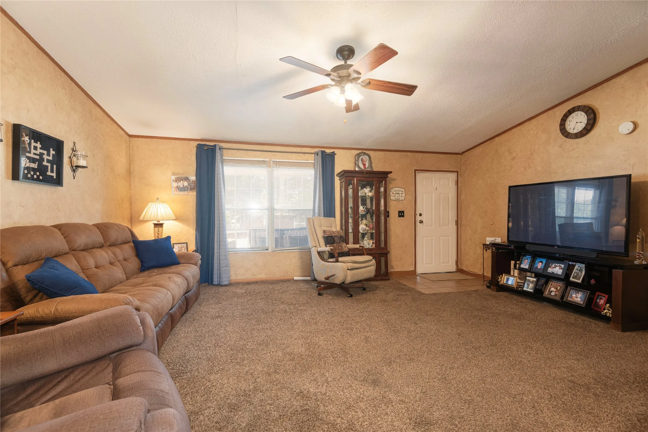Carpeted living area with a ceiling fan, a white entry door, and a built-in display cabinet