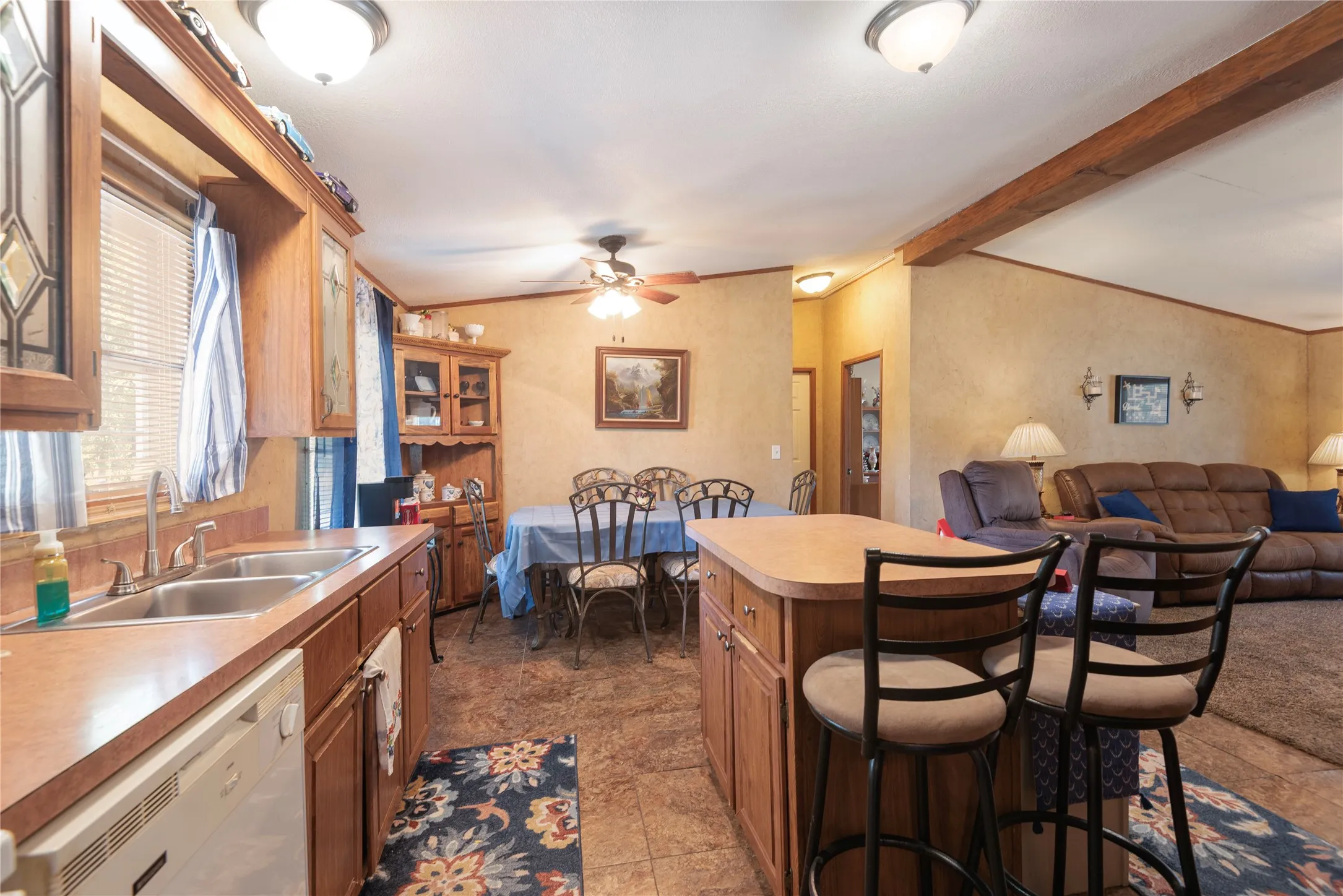 Kitchen featuring wood-finish cabinetry, a double basin sink, and a center island with bar seating