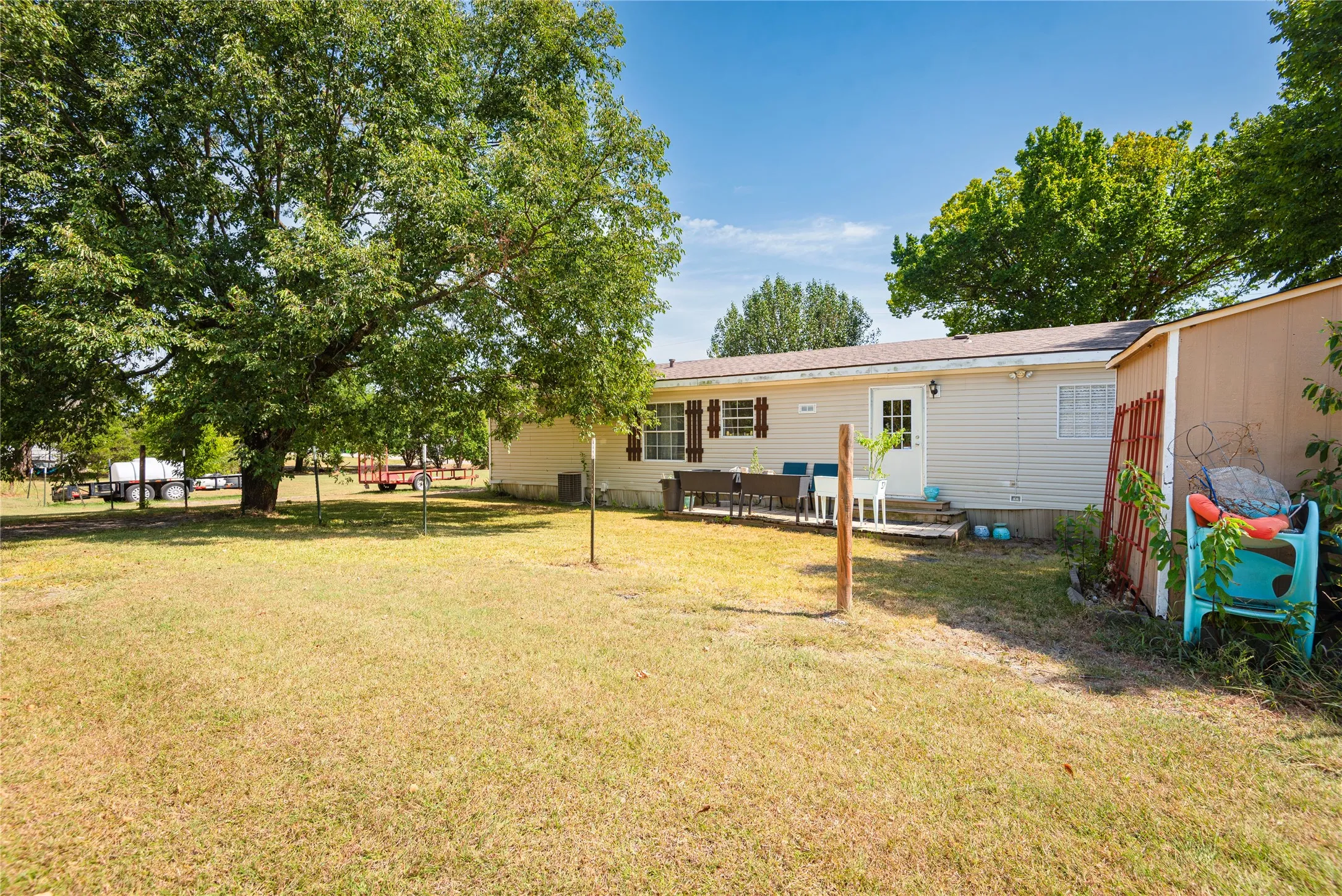 Expansive grassy yard featuring mature trees, a private patio area, and a utility shed