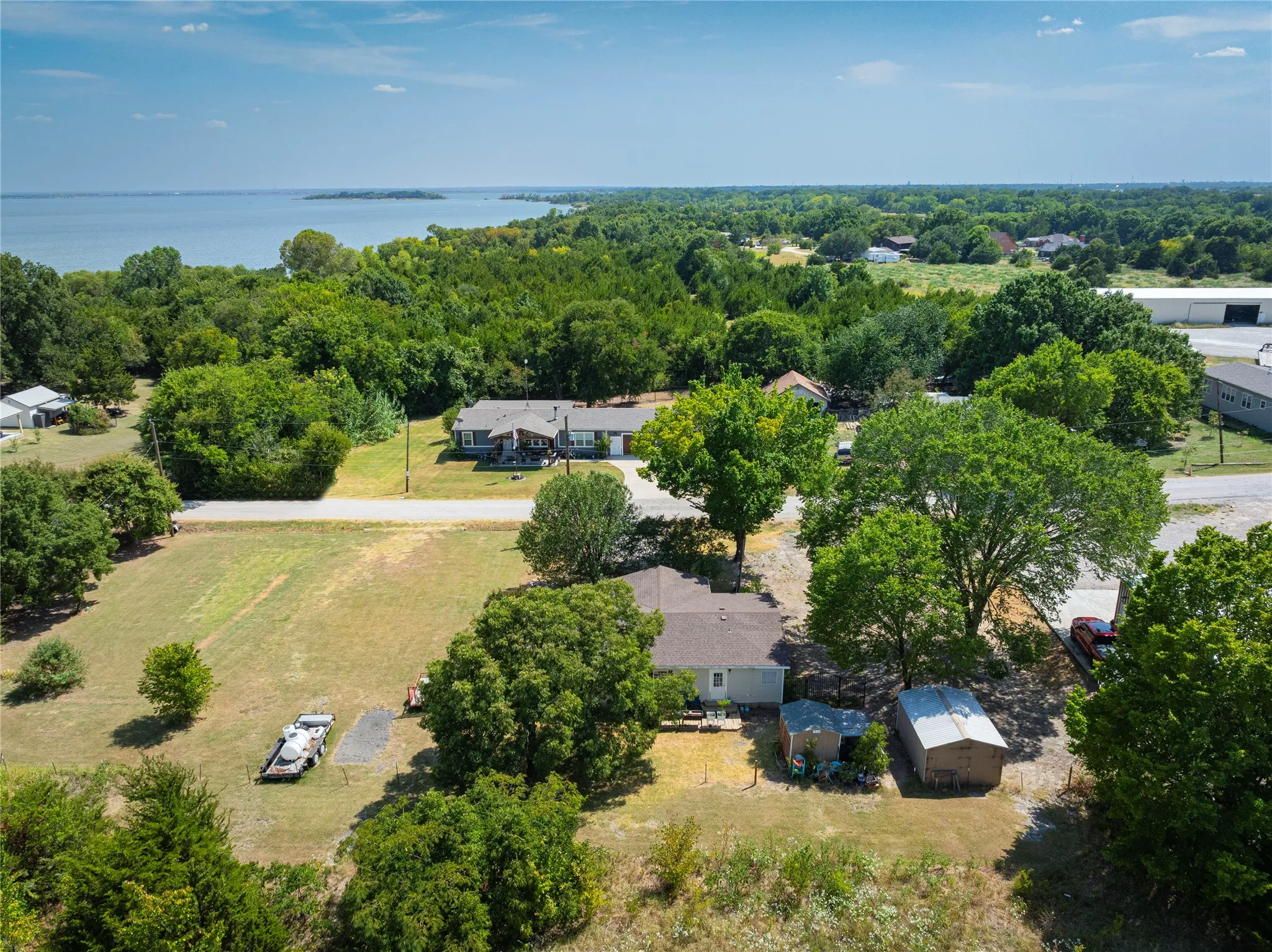 Expansive property with a large body of water at the horizon, surrounded by abundant mature trees and additional structures