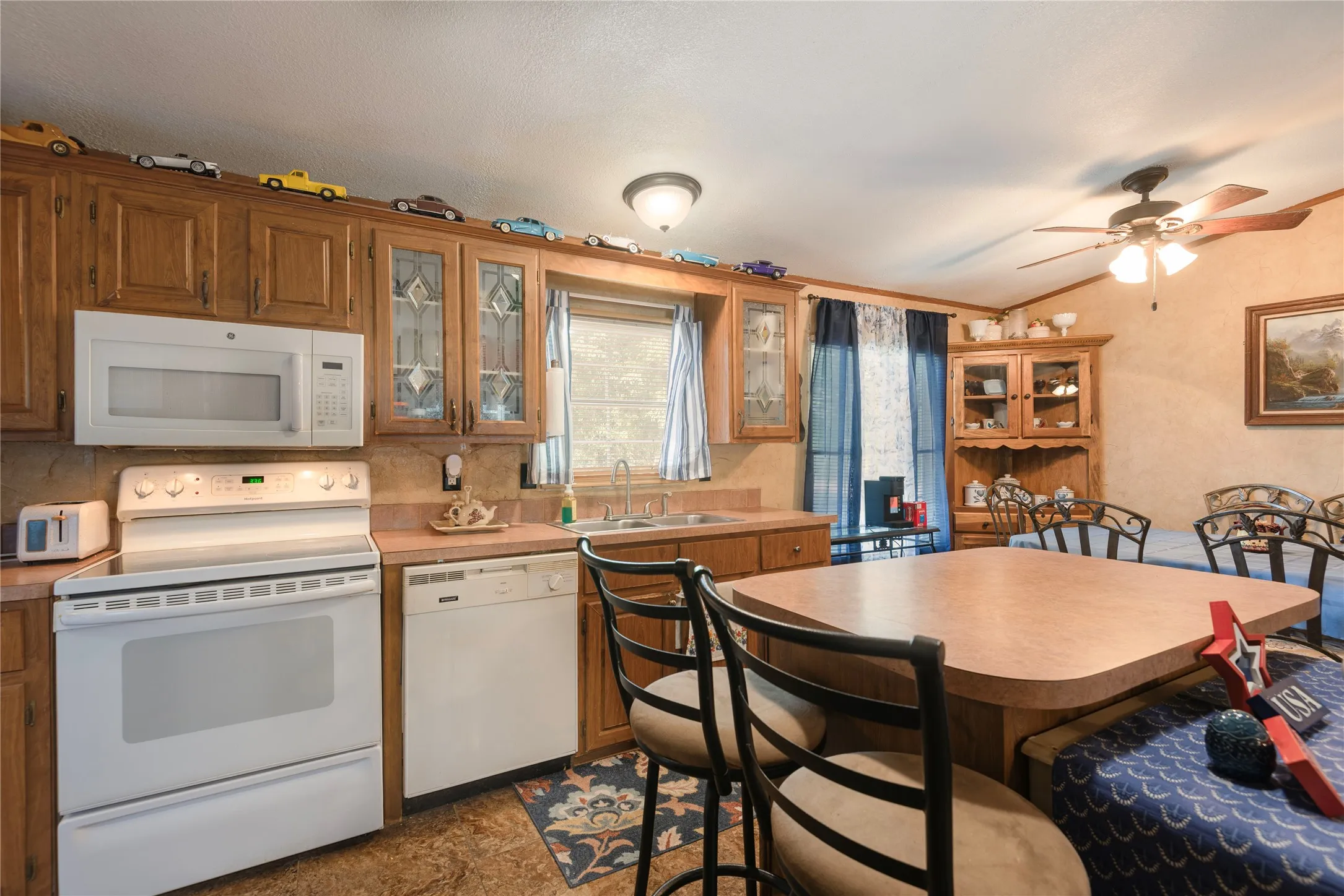 Kitchen featuring wood cabinetry, white appliances, a ceiling fan, and a built-in display cabinet