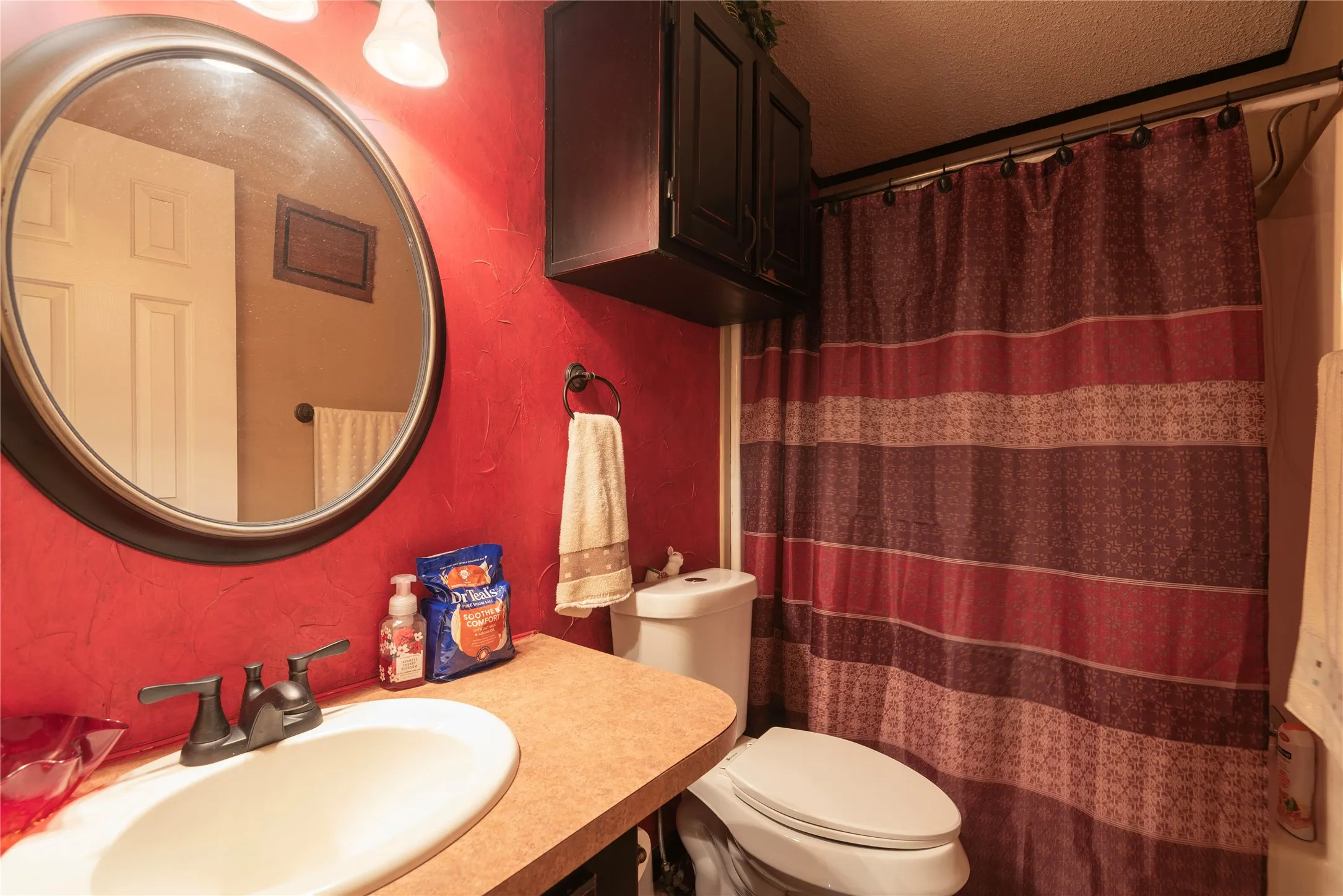 Oval vanity mirror, countertop with integrated sink, dual-handle faucet, wall-mounted storage cabinet, and shower enclosure