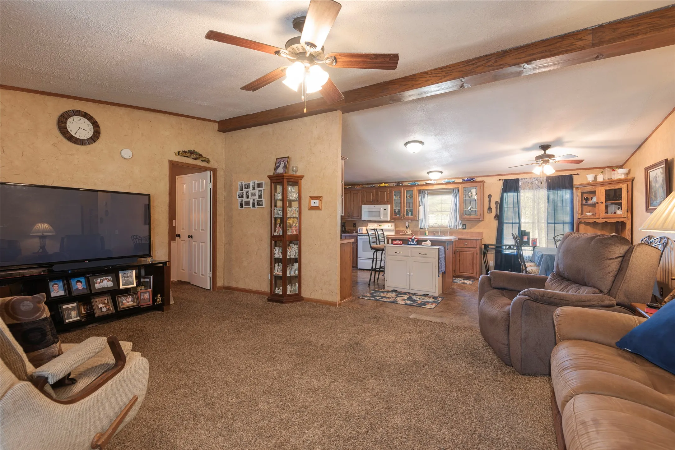 Open-concept living area with exposed wood beams, ceiling fans, and a kitchen featuring wood cabinetry and a central island