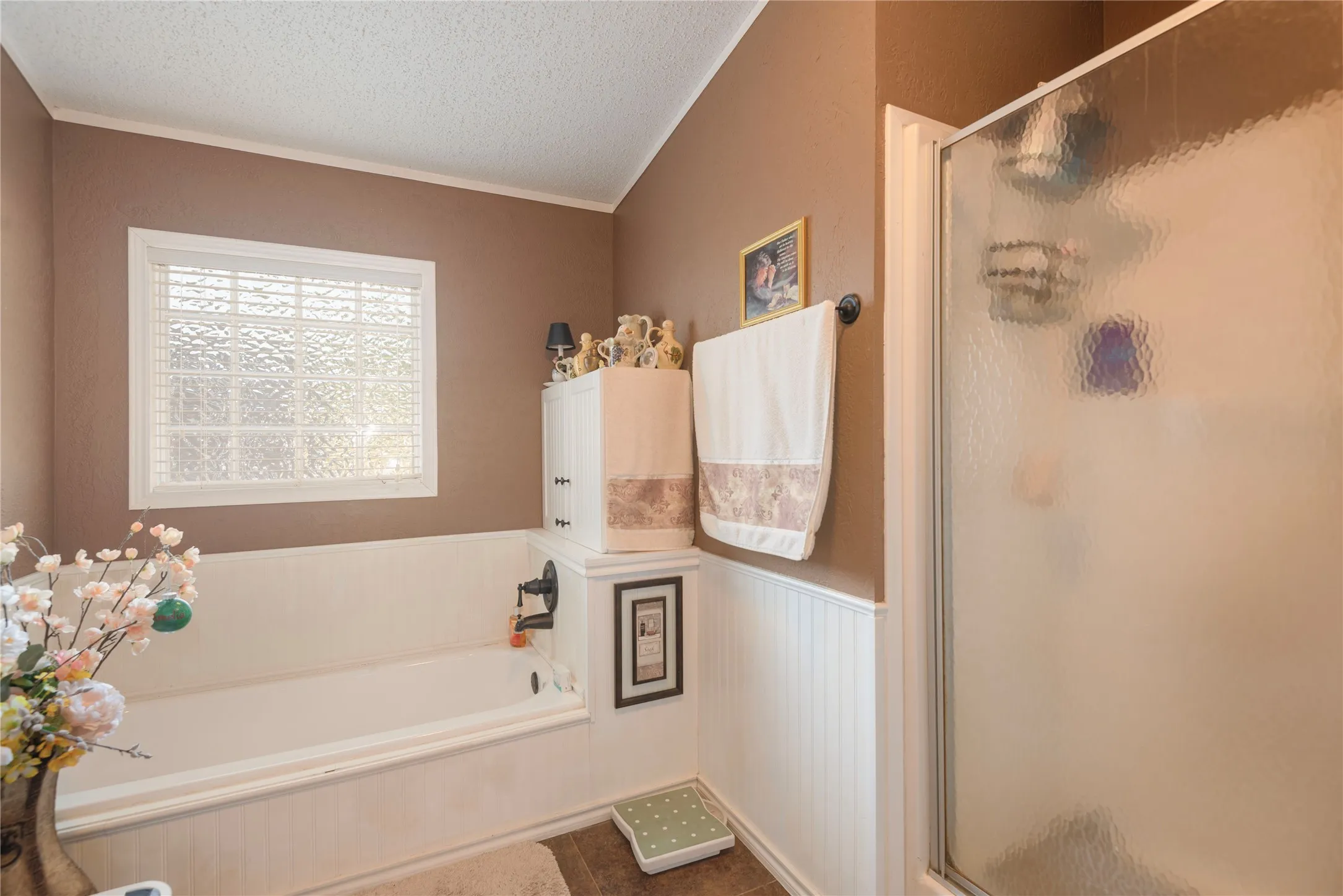 Full-size bathtub with dark bronze fixtures, frosted privacy window, white beadboard paneling, built-in cabinet storage, and a separate shower enclosure with frosted glass