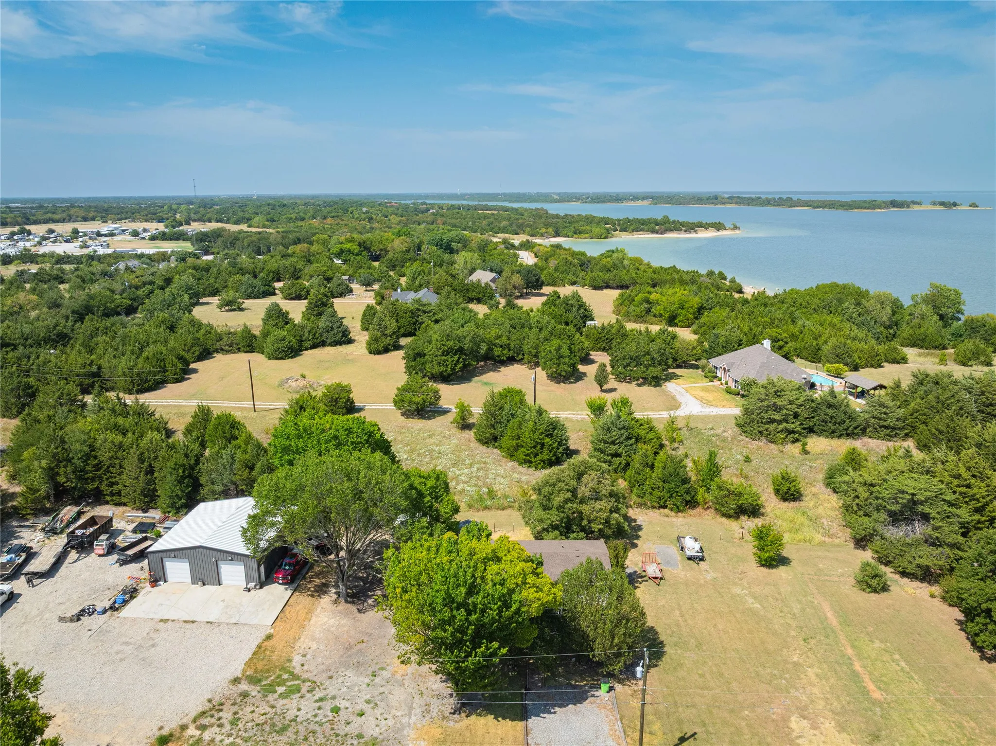 Expansive property featuring a metal-sided outbuilding with two garage bays, a gravel drive, and abundant mature trees