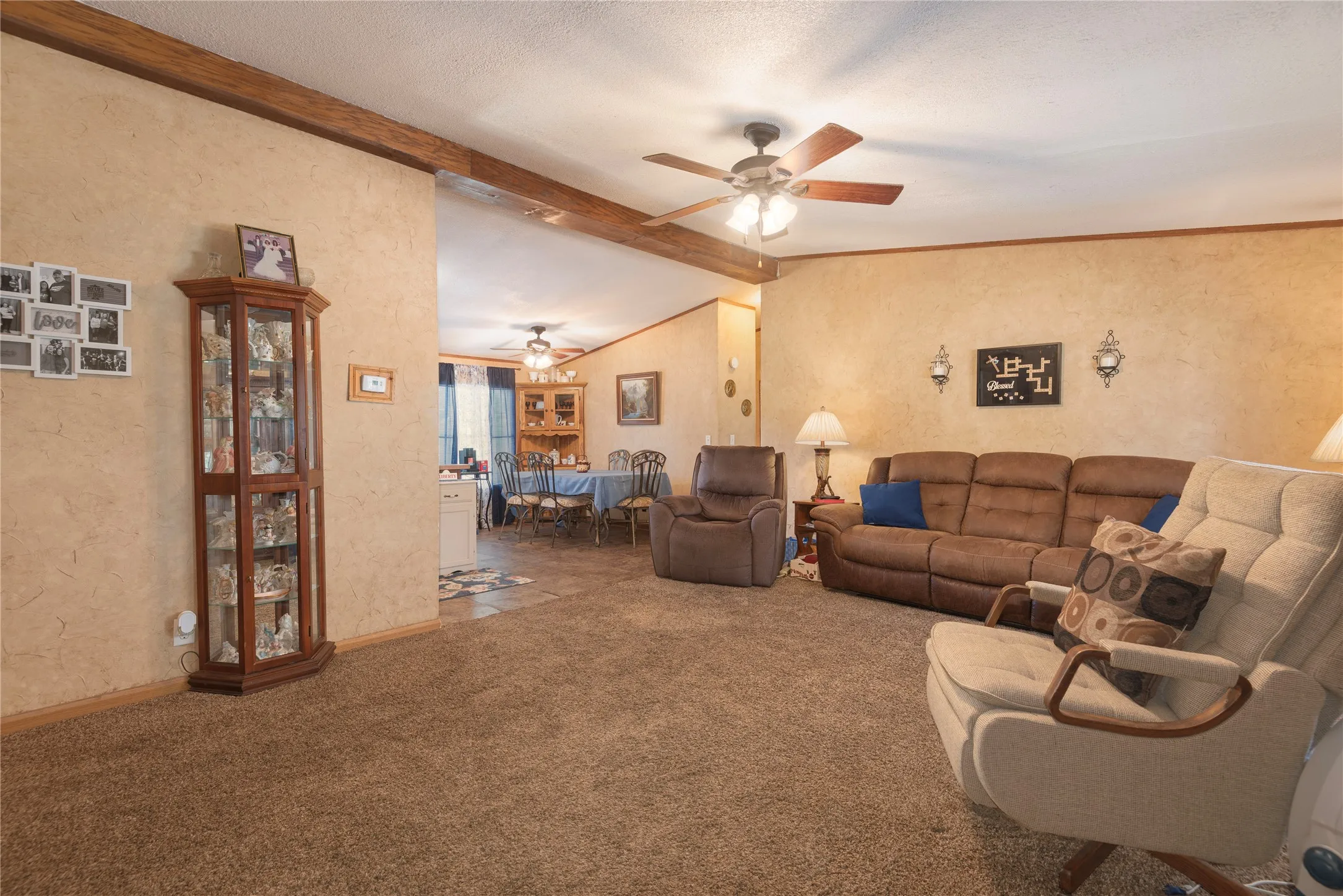 Textured wall finish, exposed wood beam, ceiling fan, carpet flooring, and tile flooring in the dining area