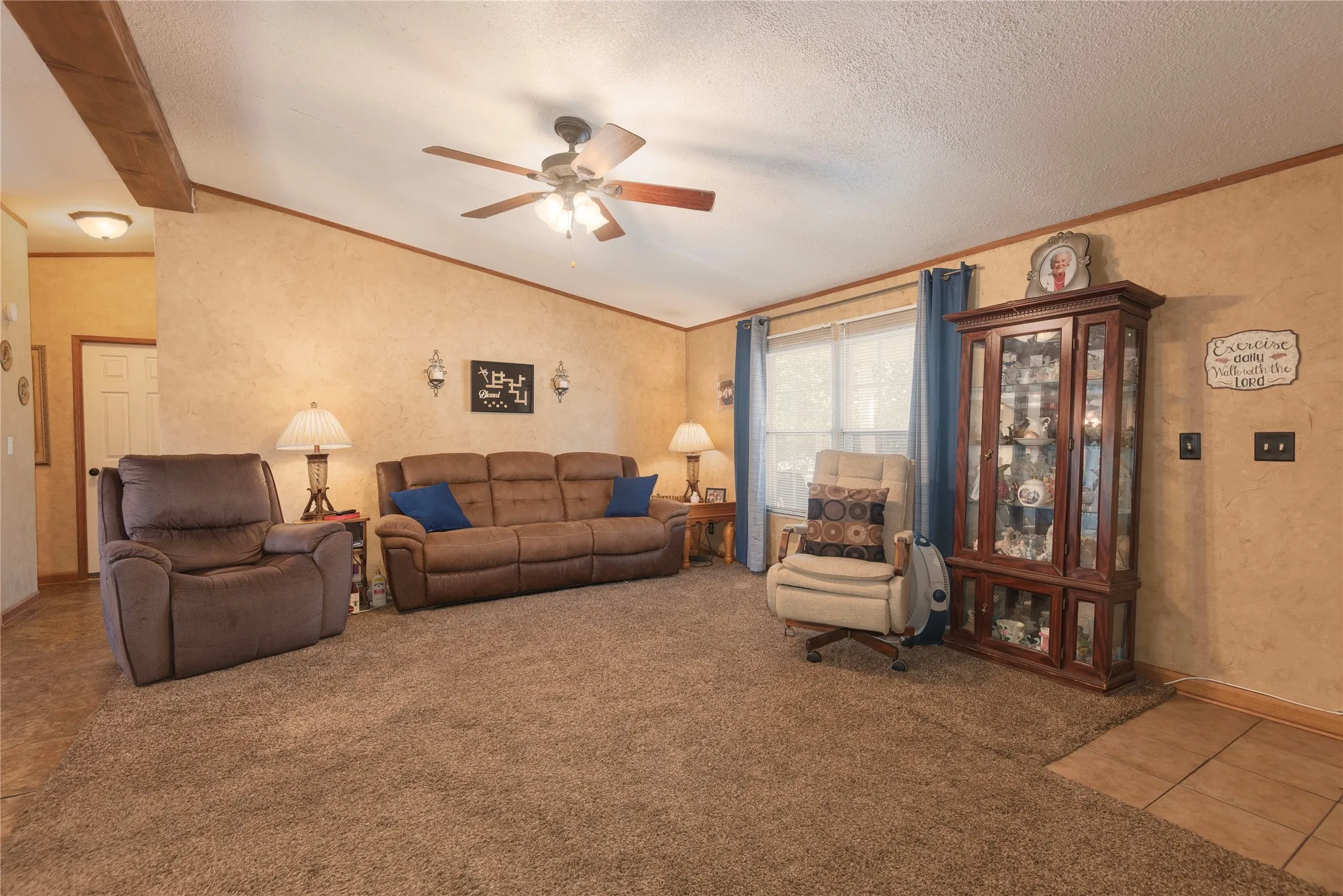 Textured wall finish, ceiling fan, architectural ceiling beam, multiple windows, and a tiled entry