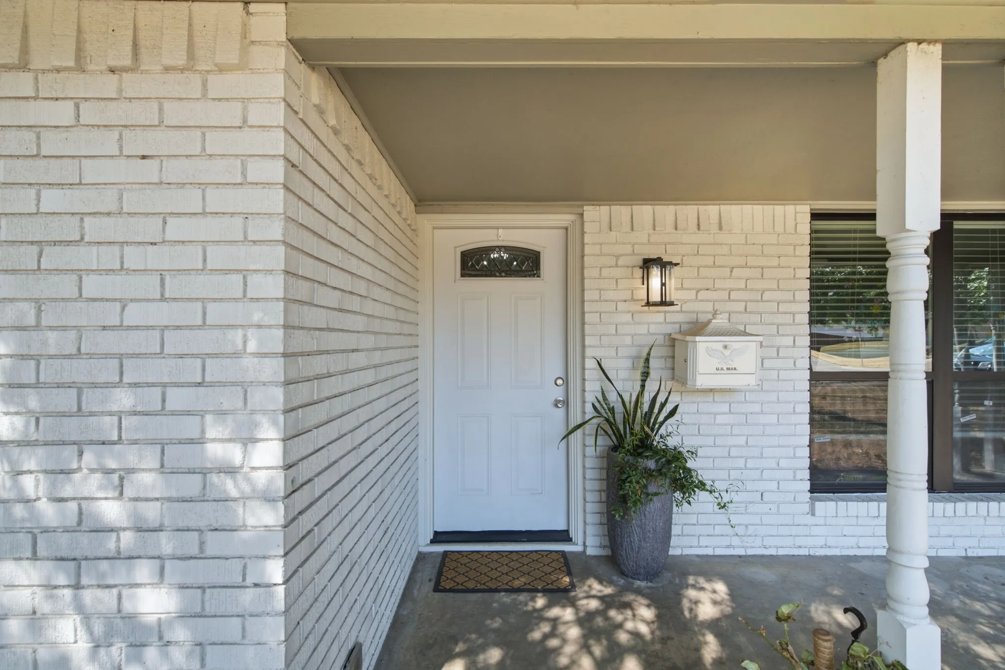 White painted brick exterior, recessed entry, decorative front door with transom, exterior wall lantern, and a wall-mounted mailbox