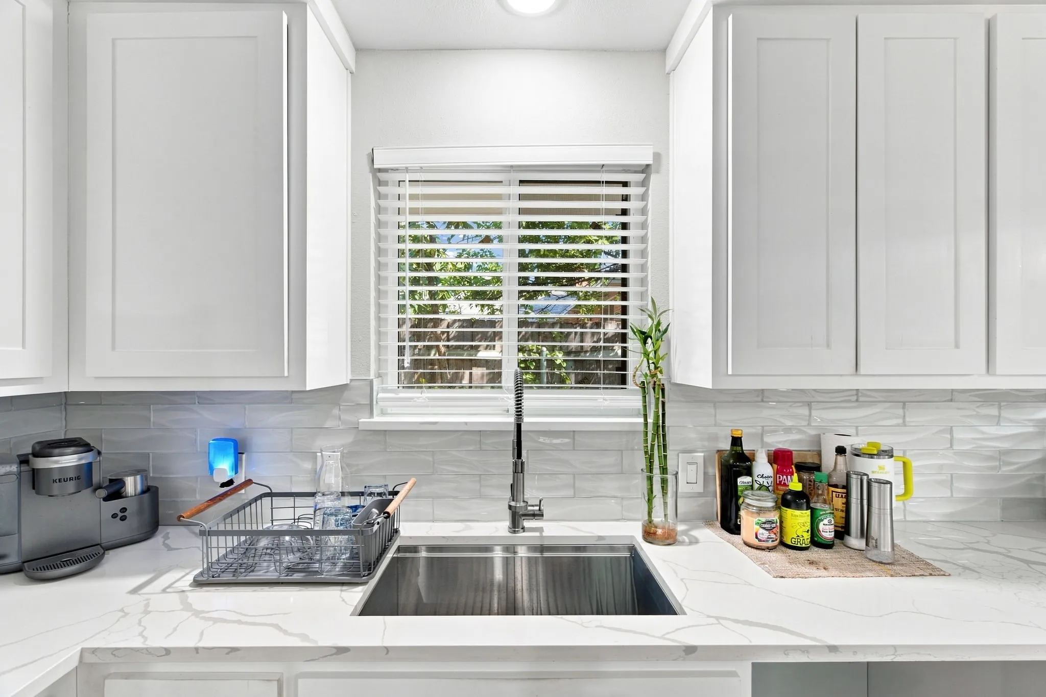Contemporary kitchen featuring white shaker-style cabinetry, linear subway tile backsplash, quartz countertops, and a stainless steel undermount sink with modern faucet