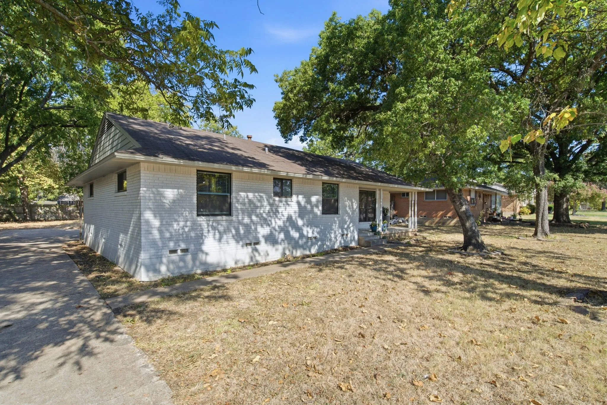White brick exterior with black-framed windows, a covered front entry, and mature trees