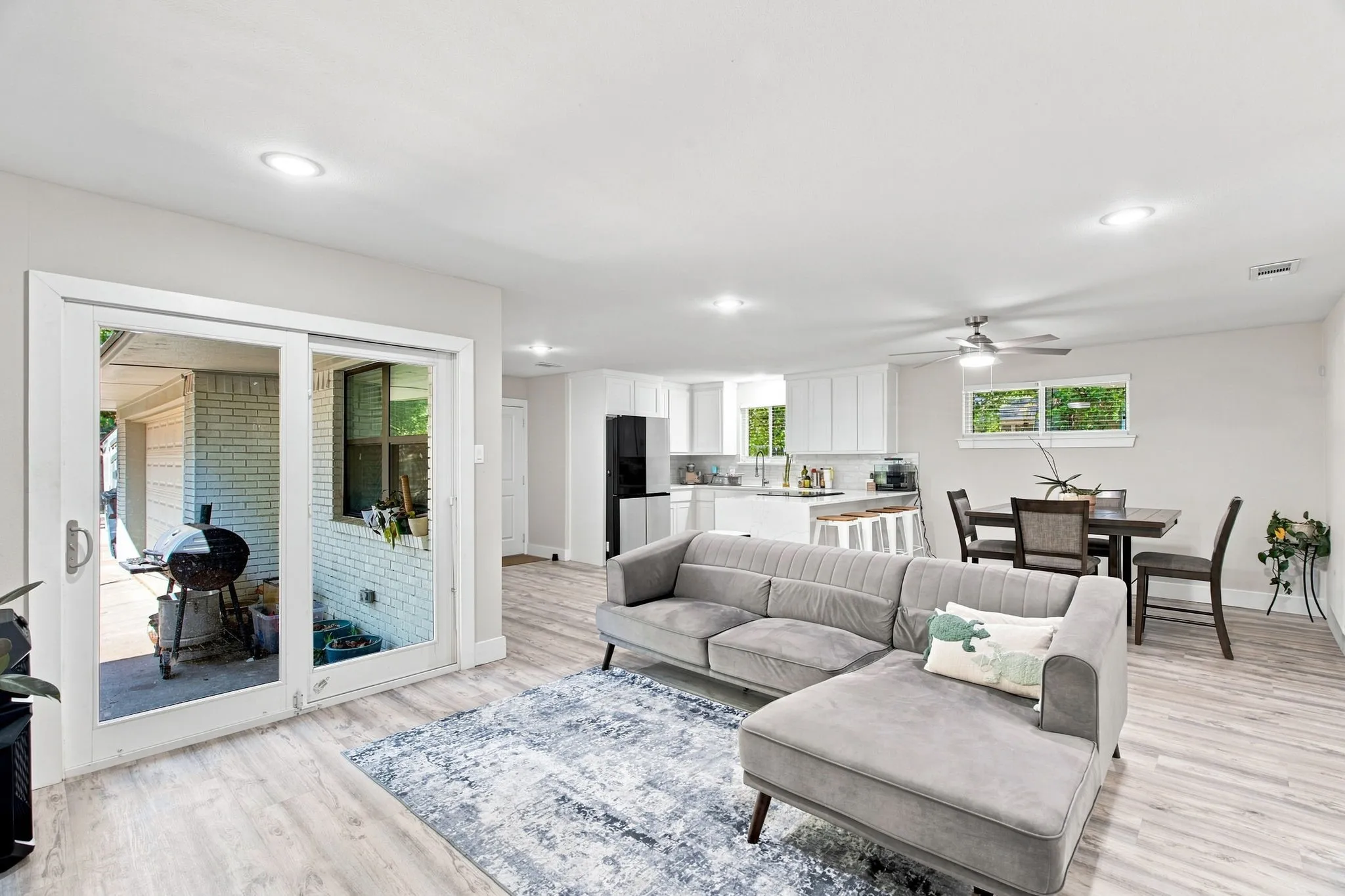 Open-concept living area featuring light wood-finish flooring throughout, a gray upholstered sectional with ottoman, recessed ceiling lighting, and ceiling fan