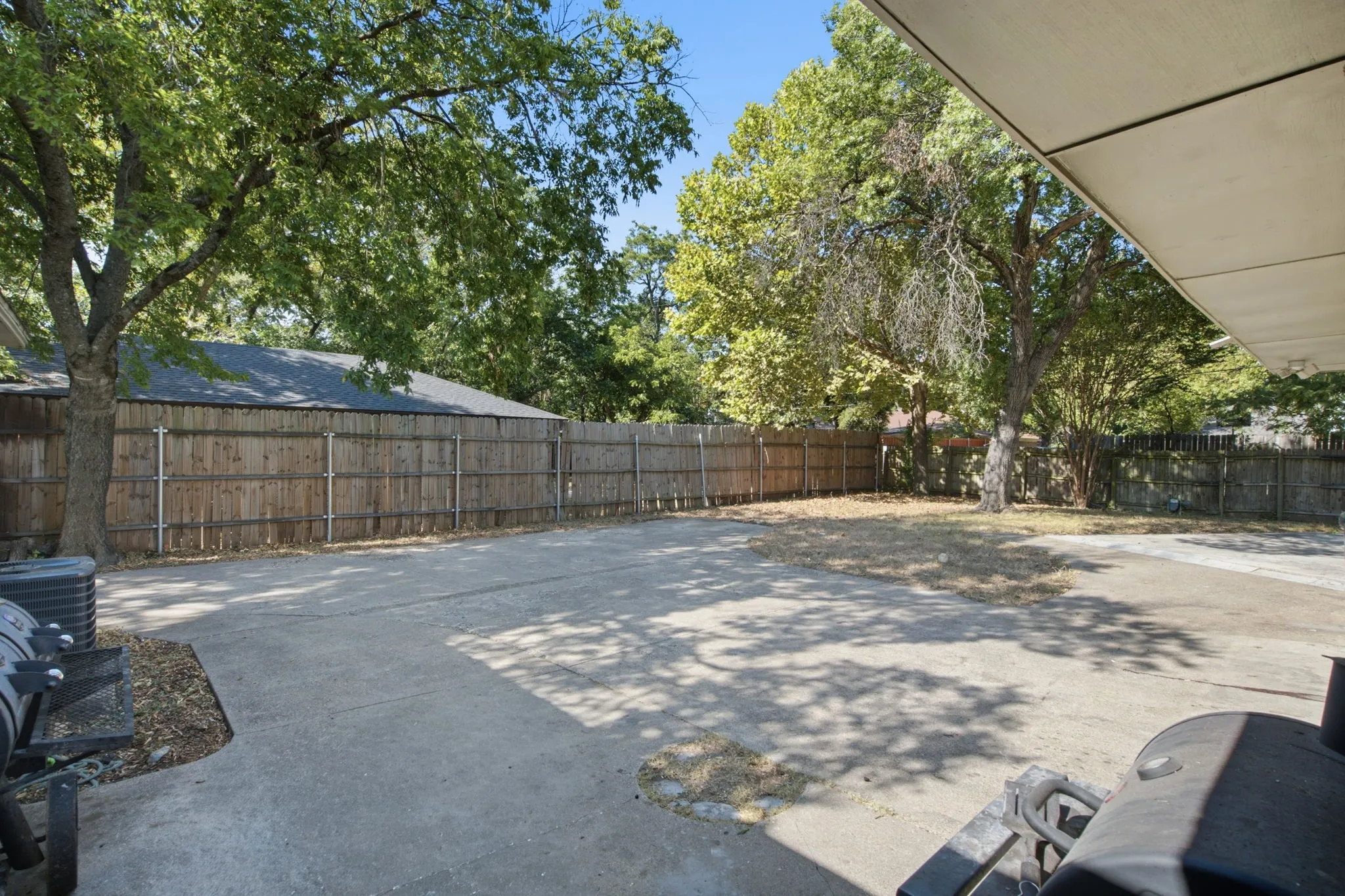 Expansive concrete patio with partial overhead coverage and a wood privacy fence
