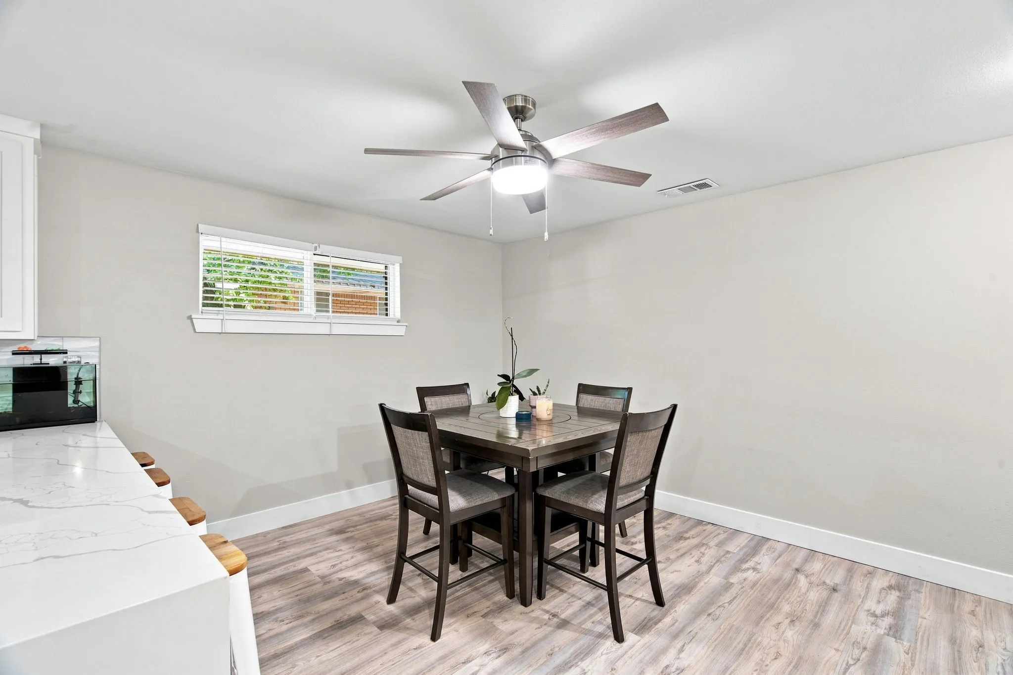 Wood-finish flooring with white baseboards, a window with horizontal blinds, and a ceiling fan with integrated lighting