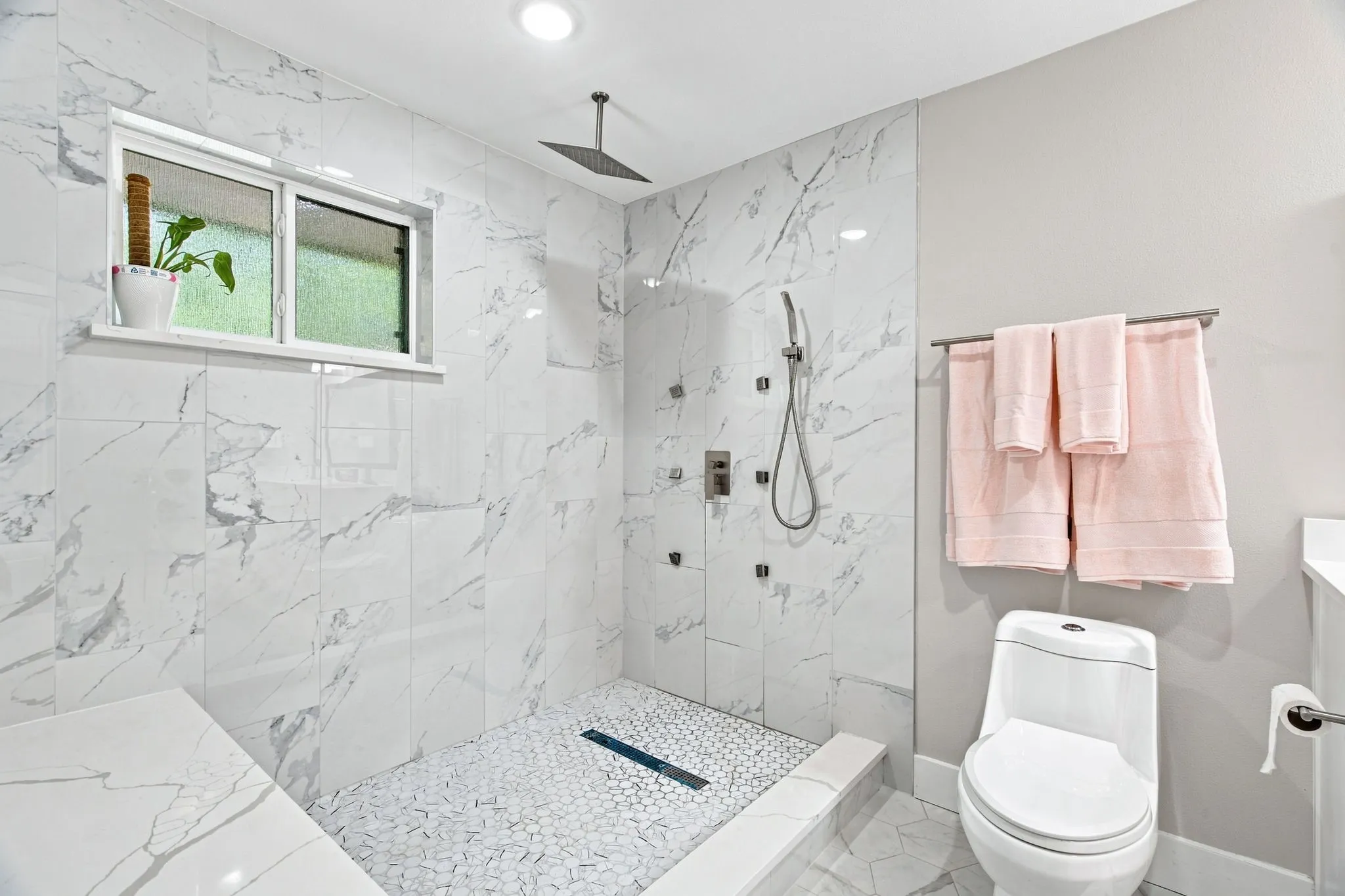 Walk-in shower with marble-look tile walls, pebble-style floor, built-in bench, and rain shower head
