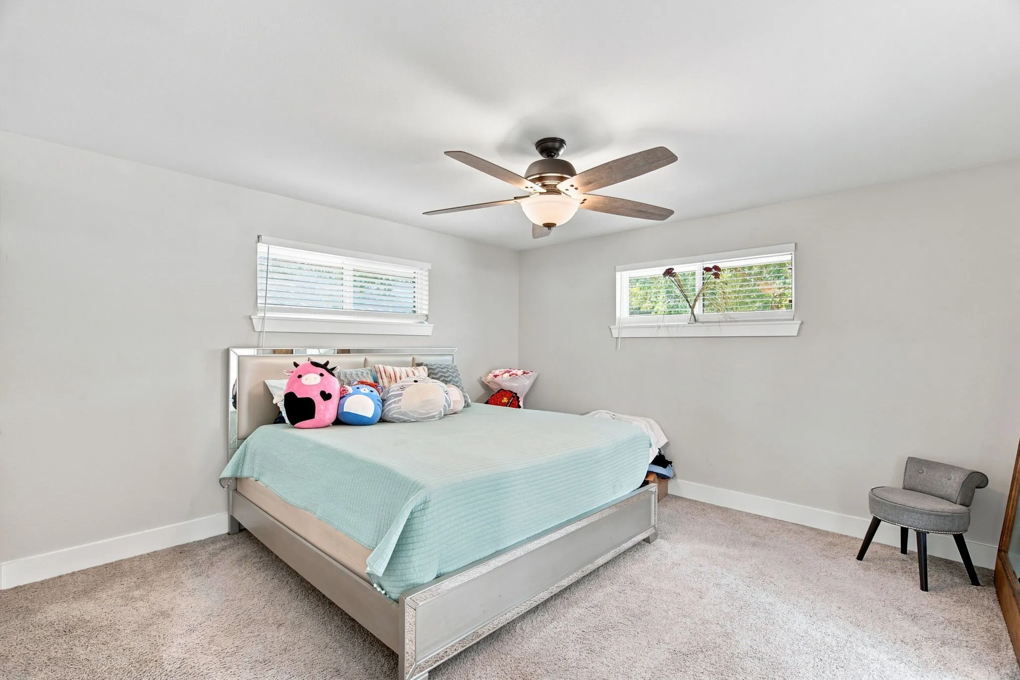 Neutral wall paint, two windows with blinds, ceiling fan with light fixture, and carpeted flooring