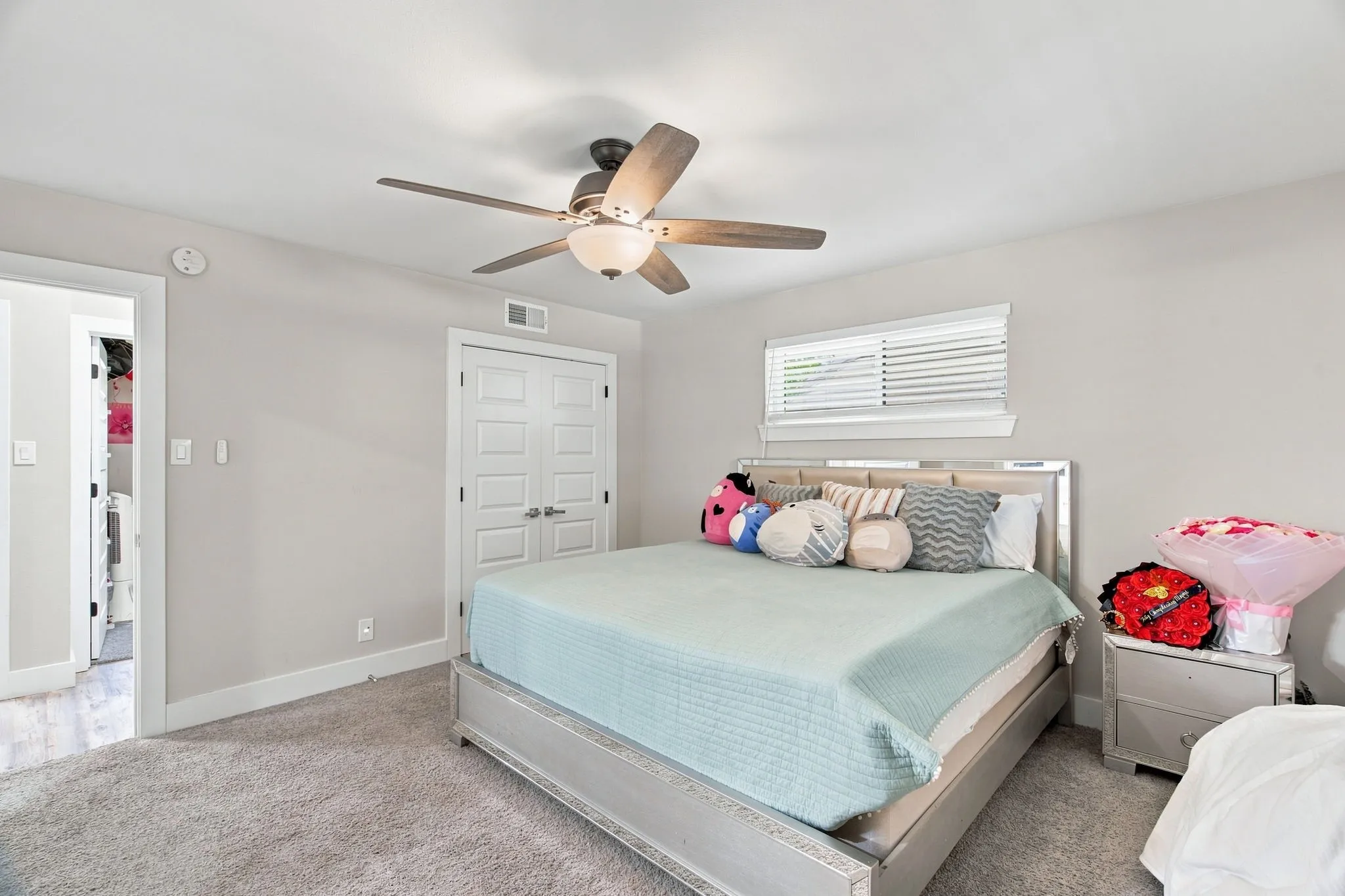 Recessed window, wood-finish ceiling fan, white paneled doors, light gray wall paint, and gray carpet flooring
