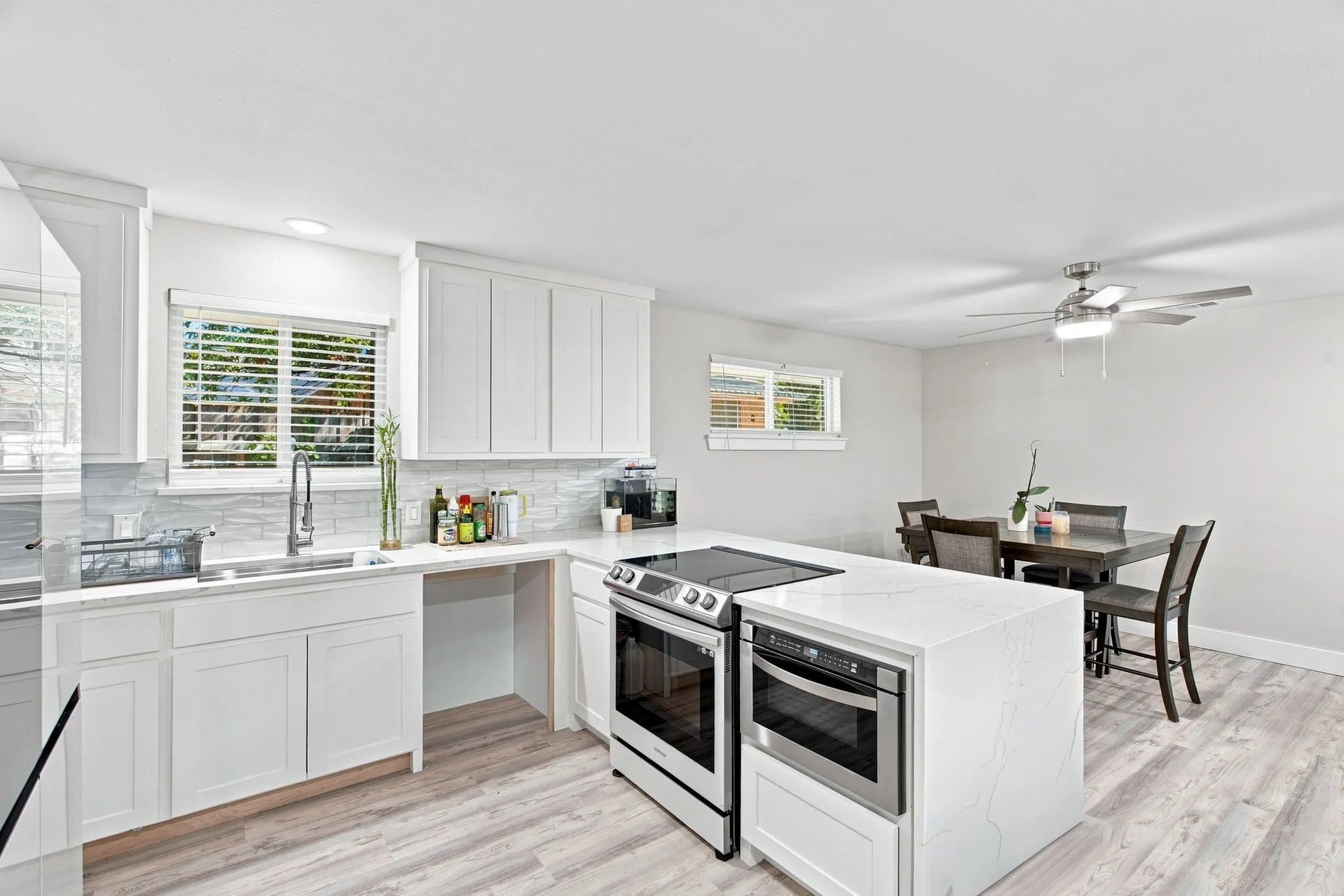 White shaker cabinetry, light-toned wood-finish flooring, white stone countertops, built-in stainless steel microwave, and a stainless steel ceiling fan