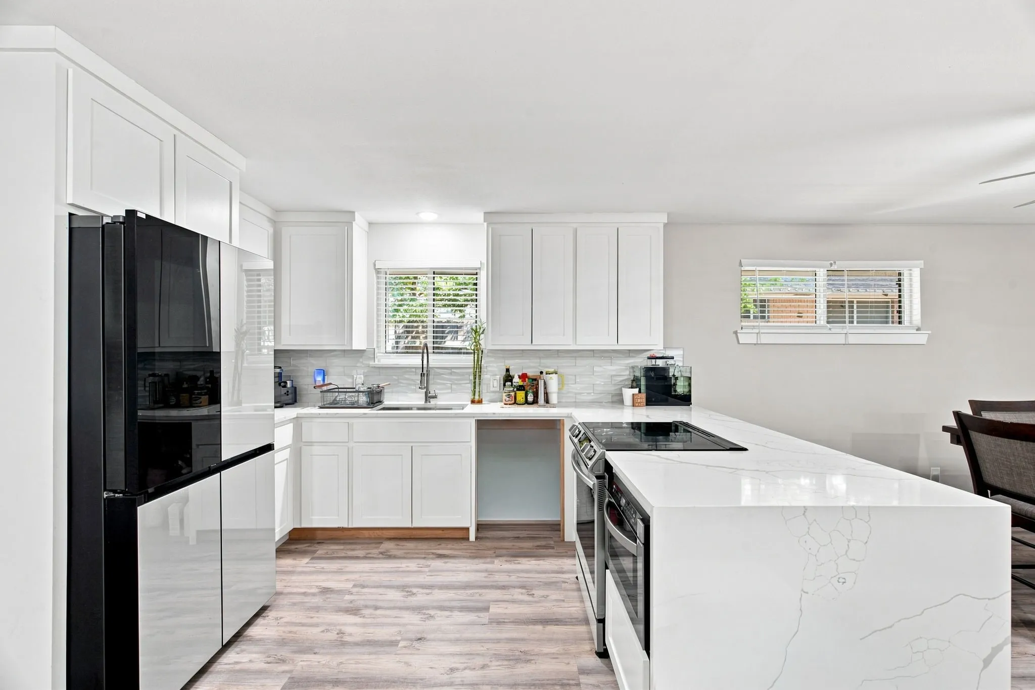 White shaker cabinetry, wood-finish flooring, white solid surface countertops, white subway tile backsplash, and a built-in cooktop