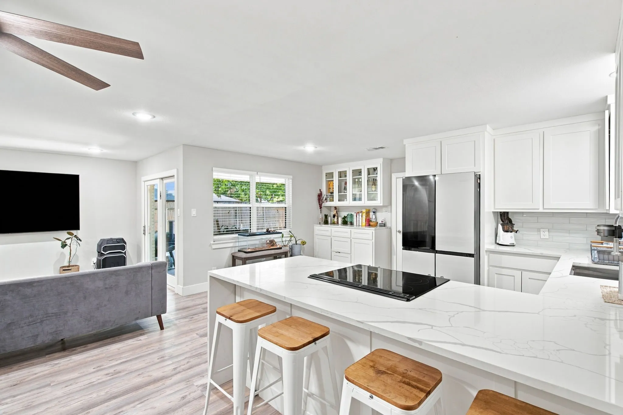 Expansive kitchen island with a built-in cooktop, white cabinetry, tile backsplash, and light wood-finish flooring