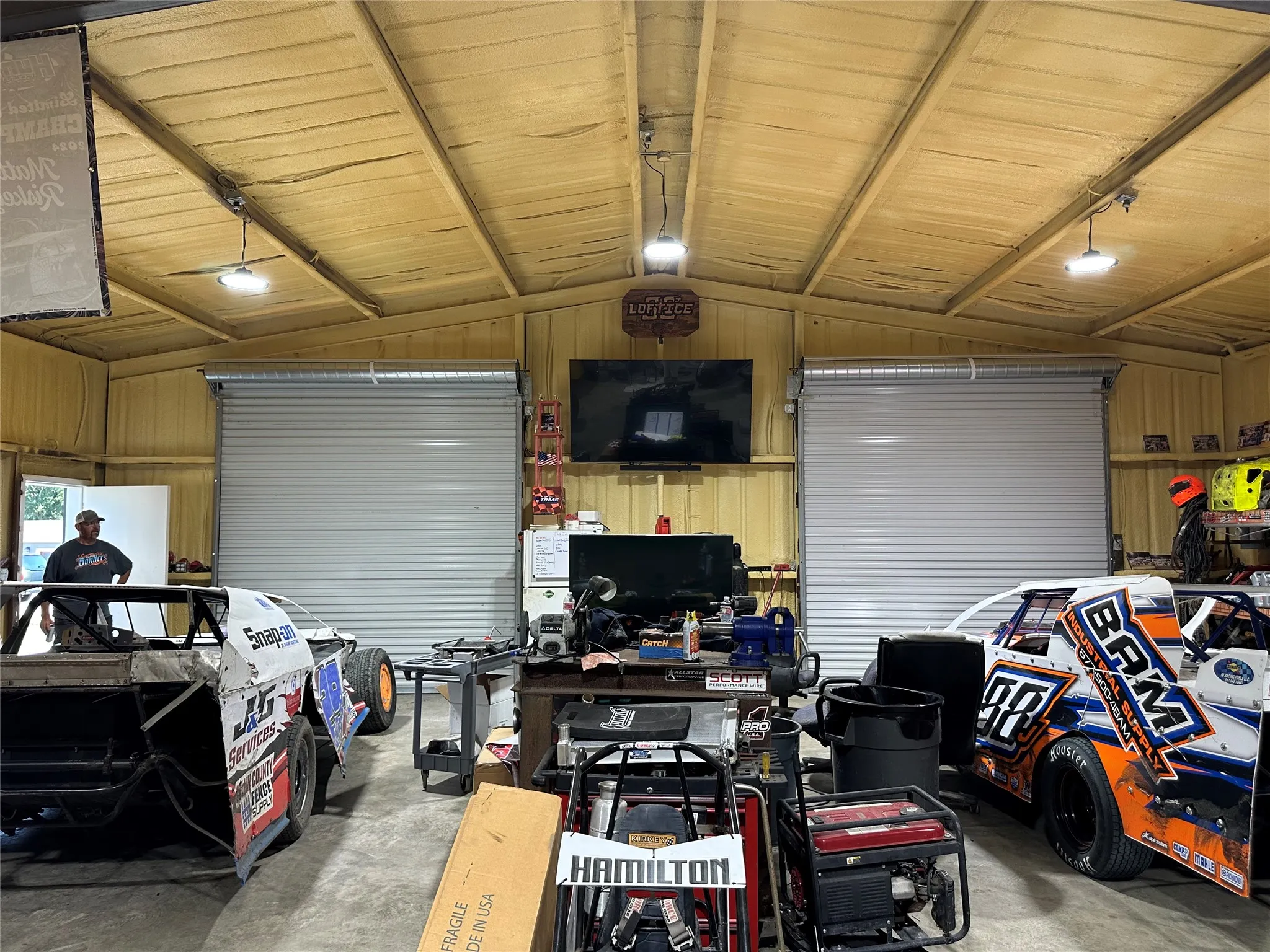 High-ceiling utility space featuring exposed metal beams, two large roll-up doors, and overhead lighting